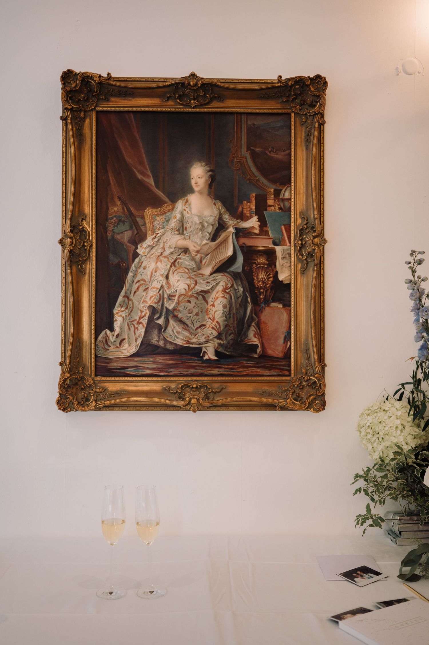 Ornate gold-framed portrait of an 18th-century noblewoman displayed above champagne glasses.