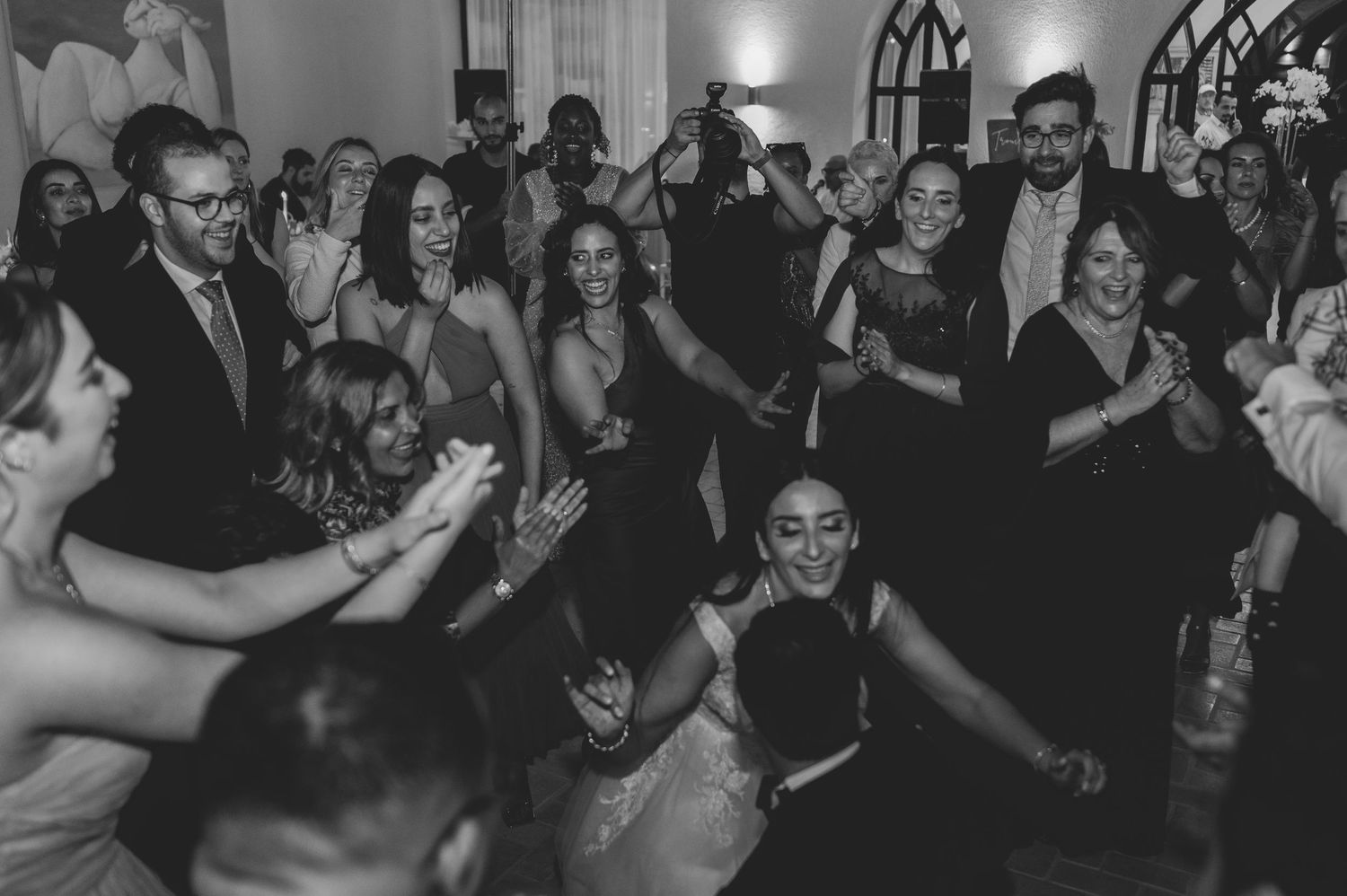 Black and white photo of wedding guests dancing and clapping together on reception dance floor.