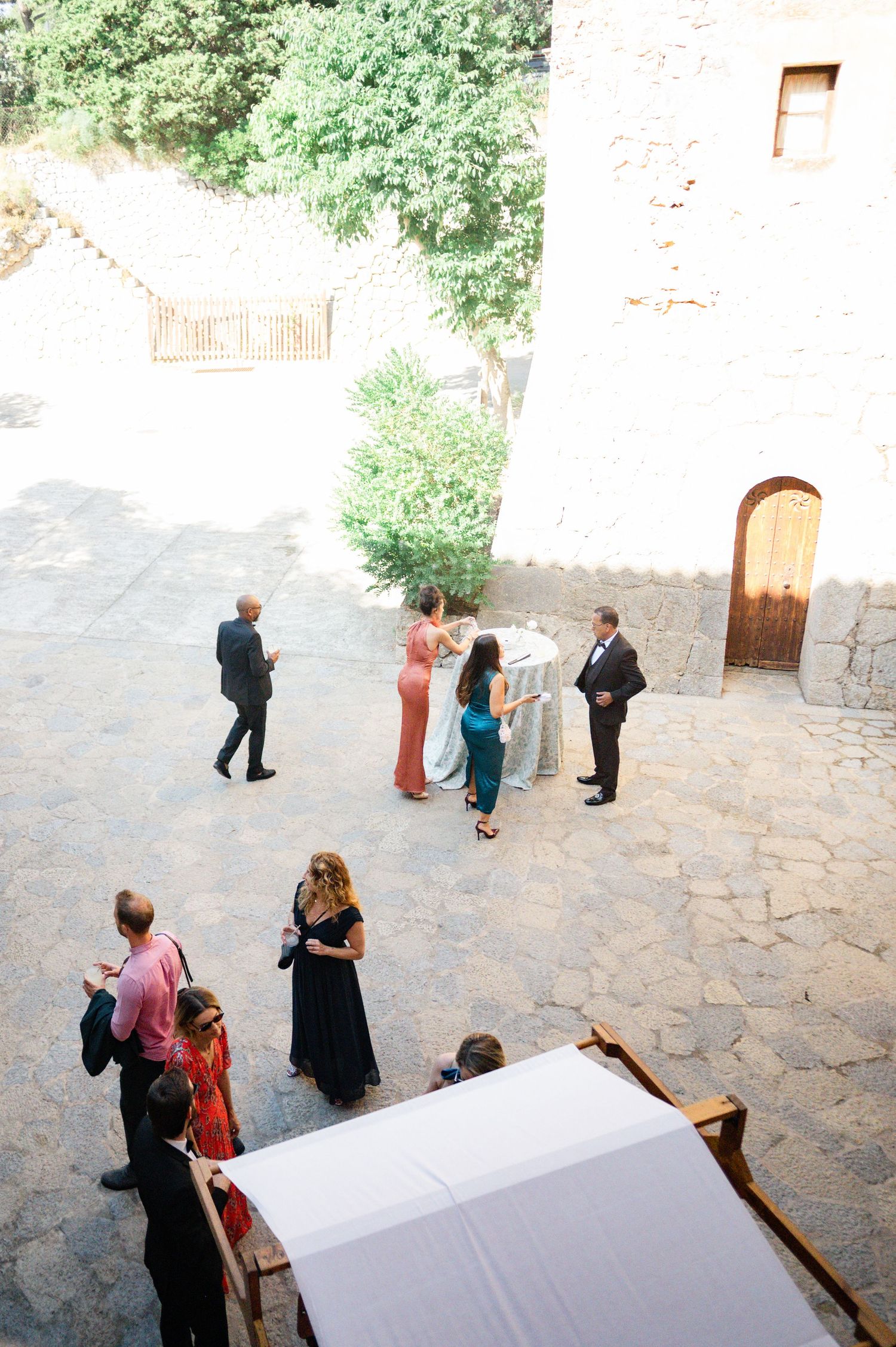 Aerial view of wedding guests arriving in sunlit stone courtyard of historic venue.