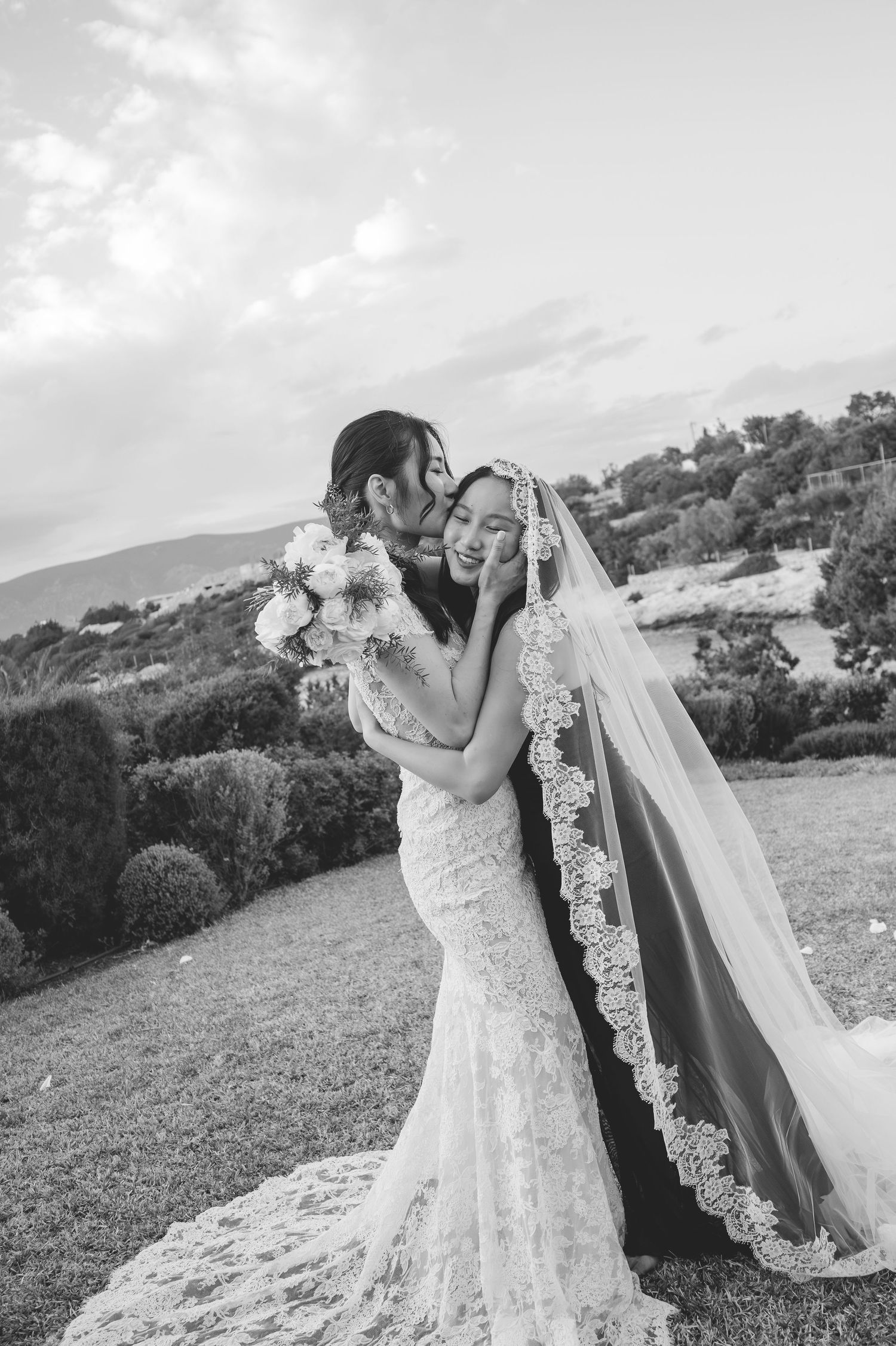 Black and white portrait of newlyweds sharing romantic moment with bride in lace gown and veil.