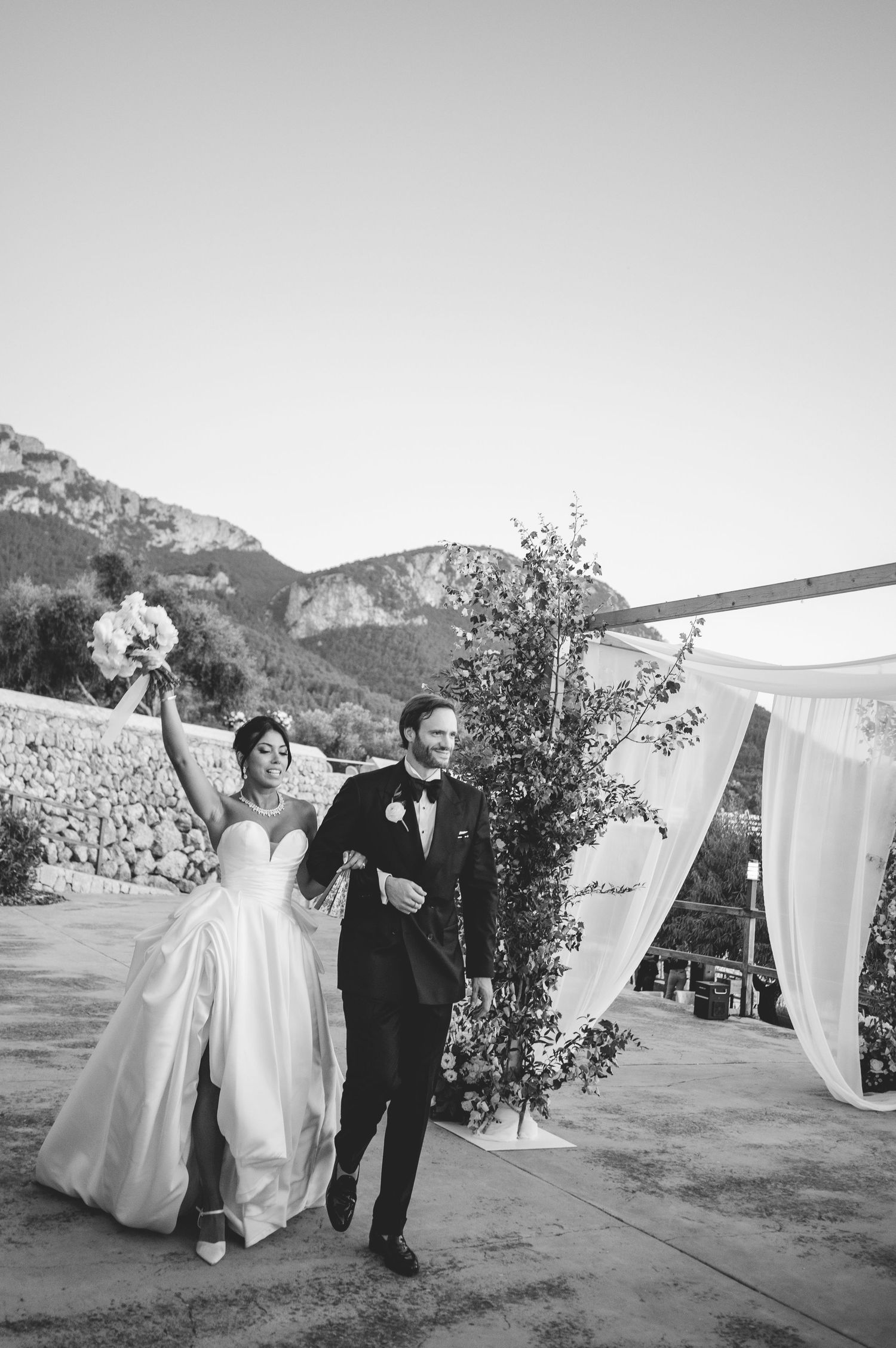 Bride and groom celebrate just married walking arm in arm at outdoor wedding ceremony with mountain backdrop.
