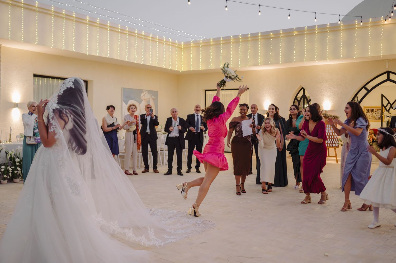 Excited guest in pink dress jumping to catch the bridal bouquet toss at wedding.