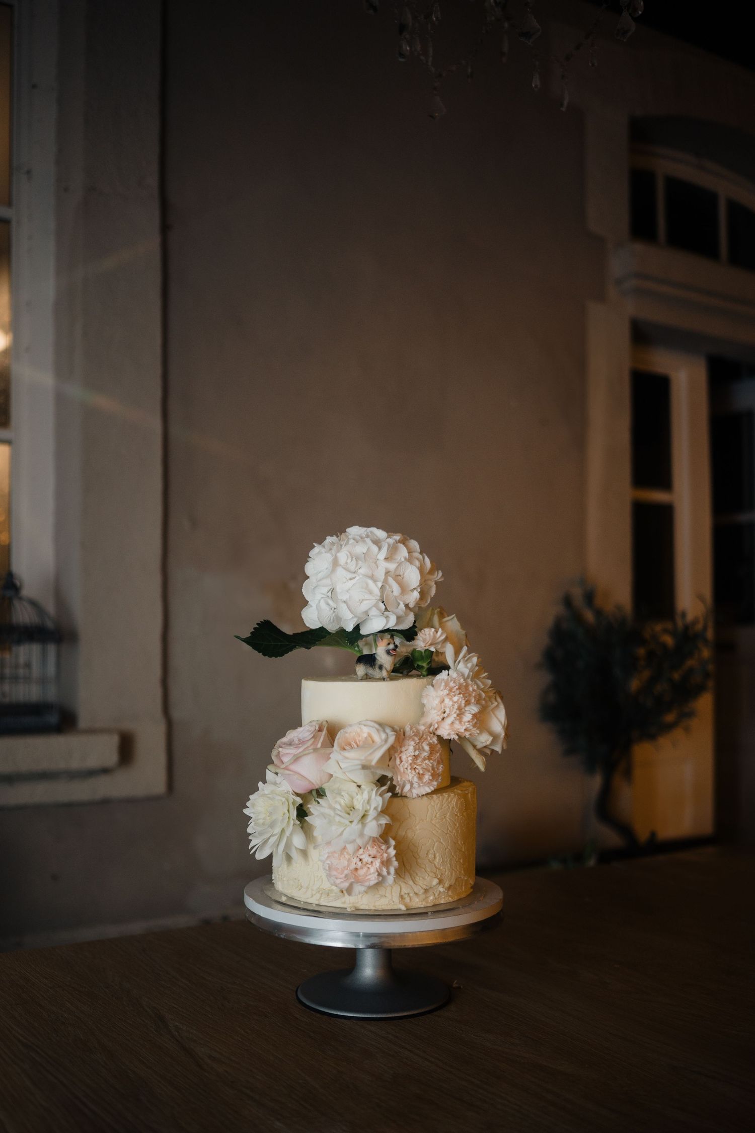 Elegant two-tier wedding cake decorated with white and blush pink flowers on a silver cake stand.