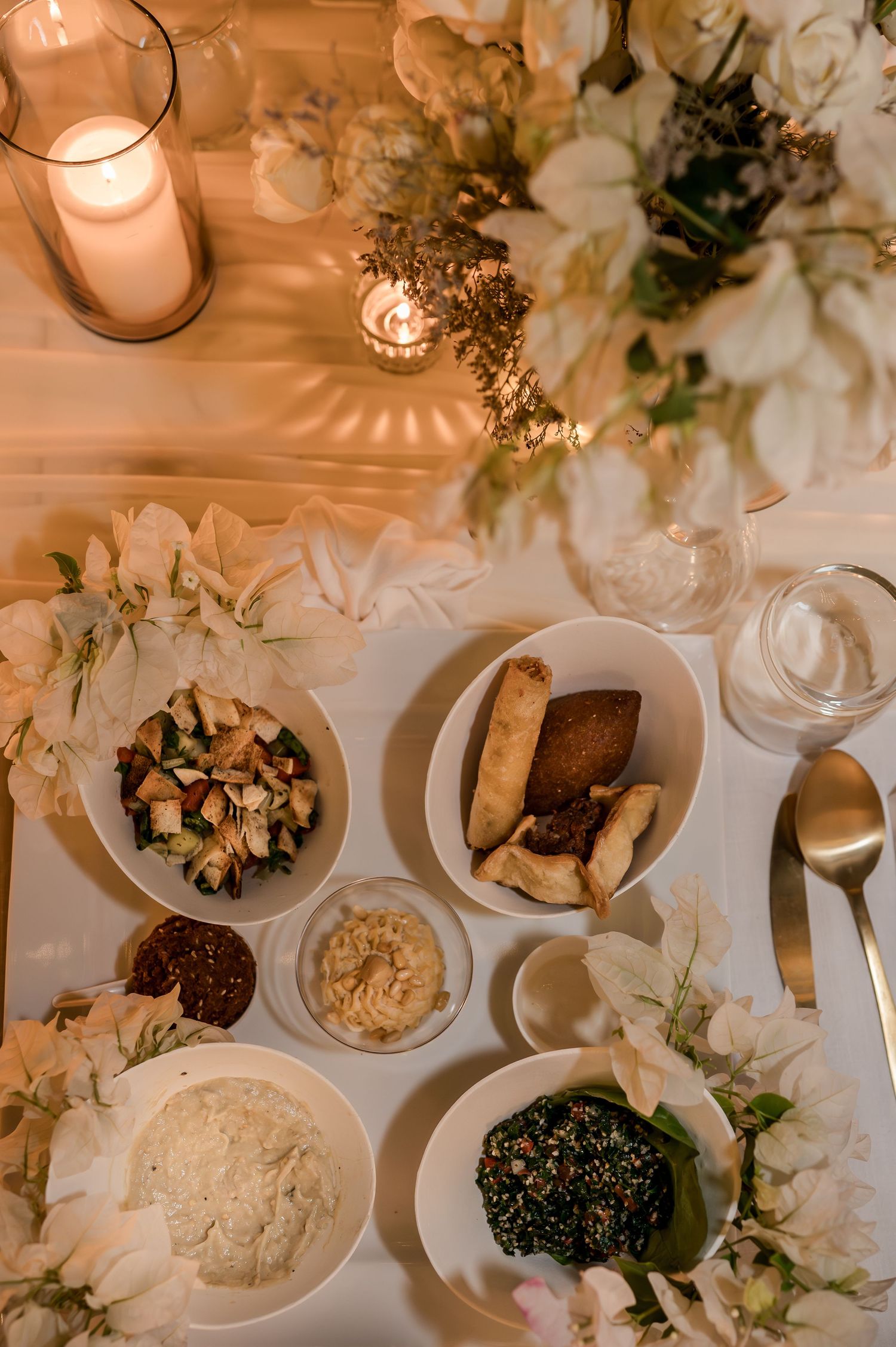 Overhead view of wedding dinner table with white flowers, candles, and assorted Middle Eastern dishes.