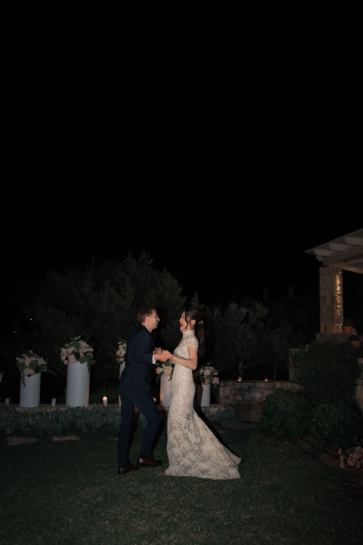 Bride and groom sharing a romantic first dance outdoors at night with floral arrangements.