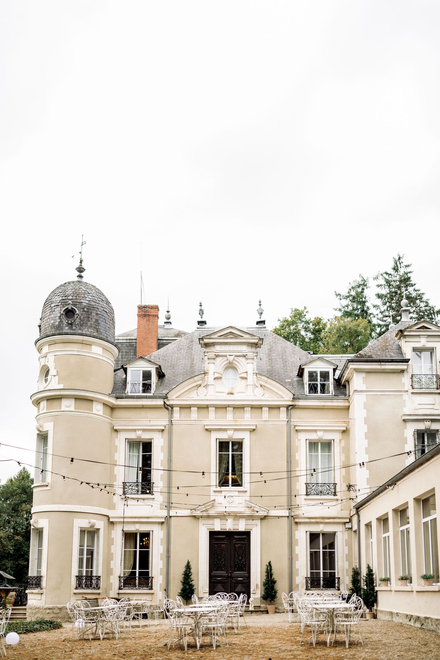 Elegant French chateau wedding venue with white outdoor furniture and string lights.