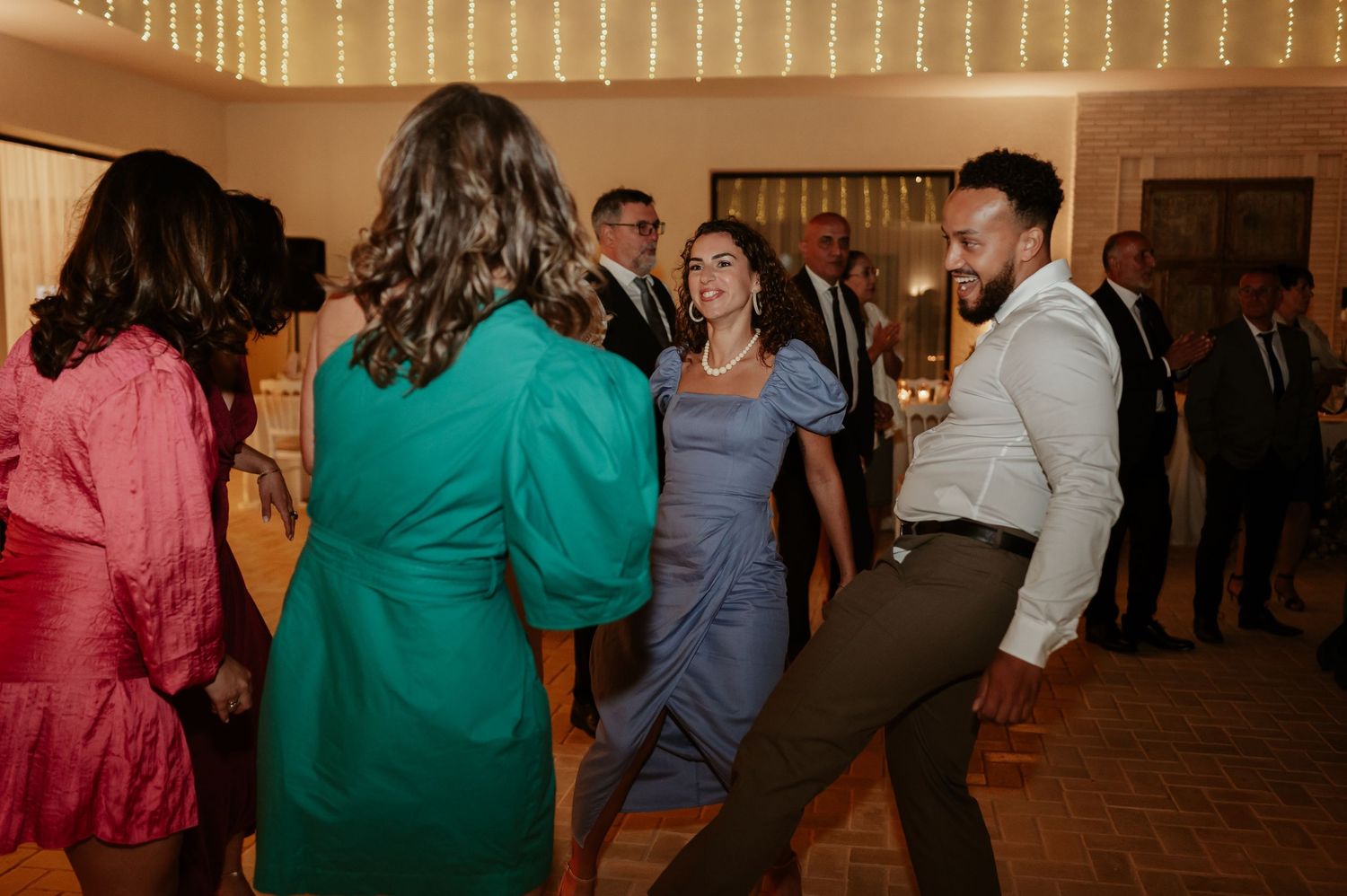 Wedding guests dance joyfully together at colorful indoor wedding reception celebration.
