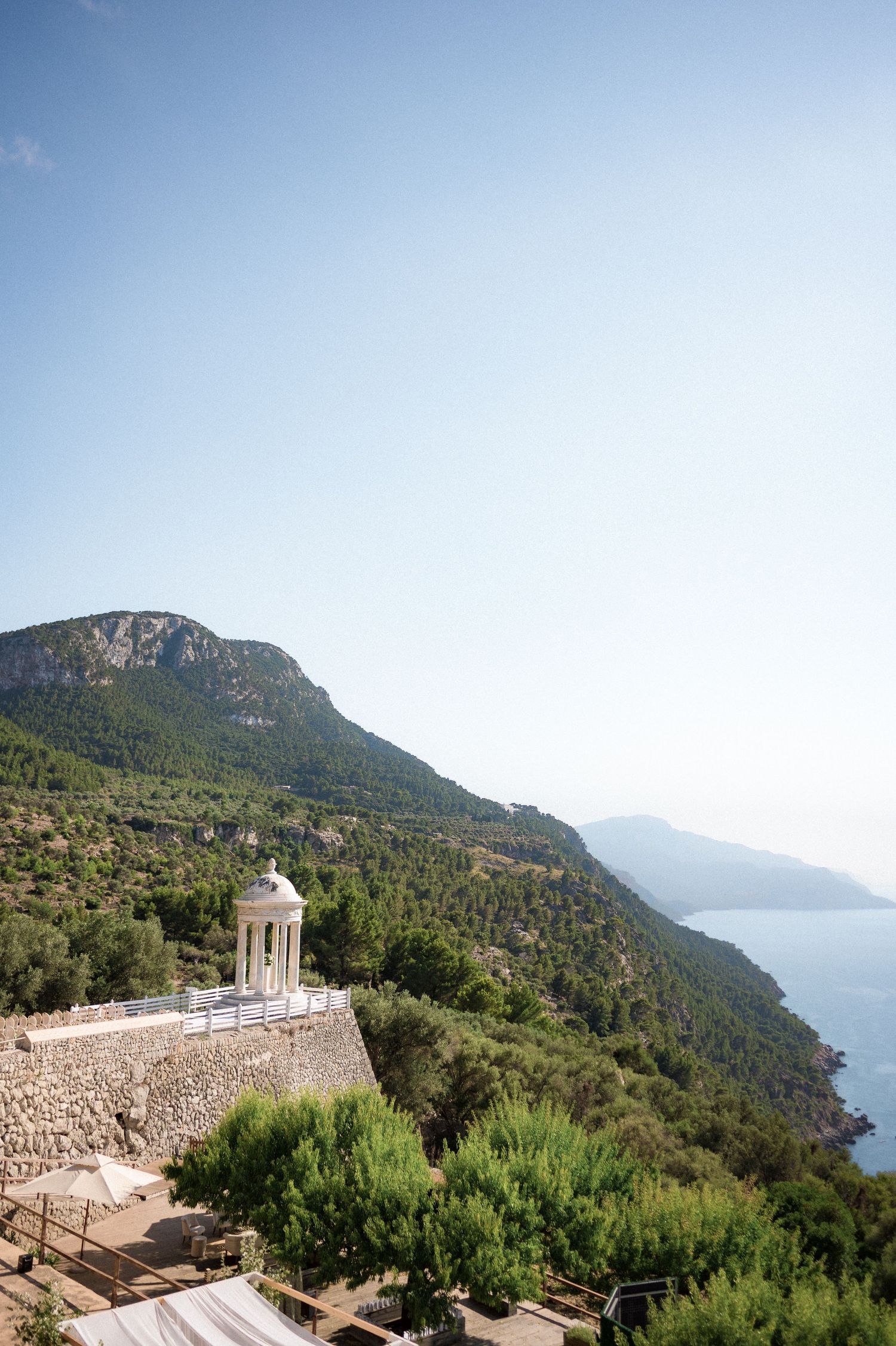 Stunning Mediterranean hillside wedding venue with white gazebo, lush greenery, and sea views.
