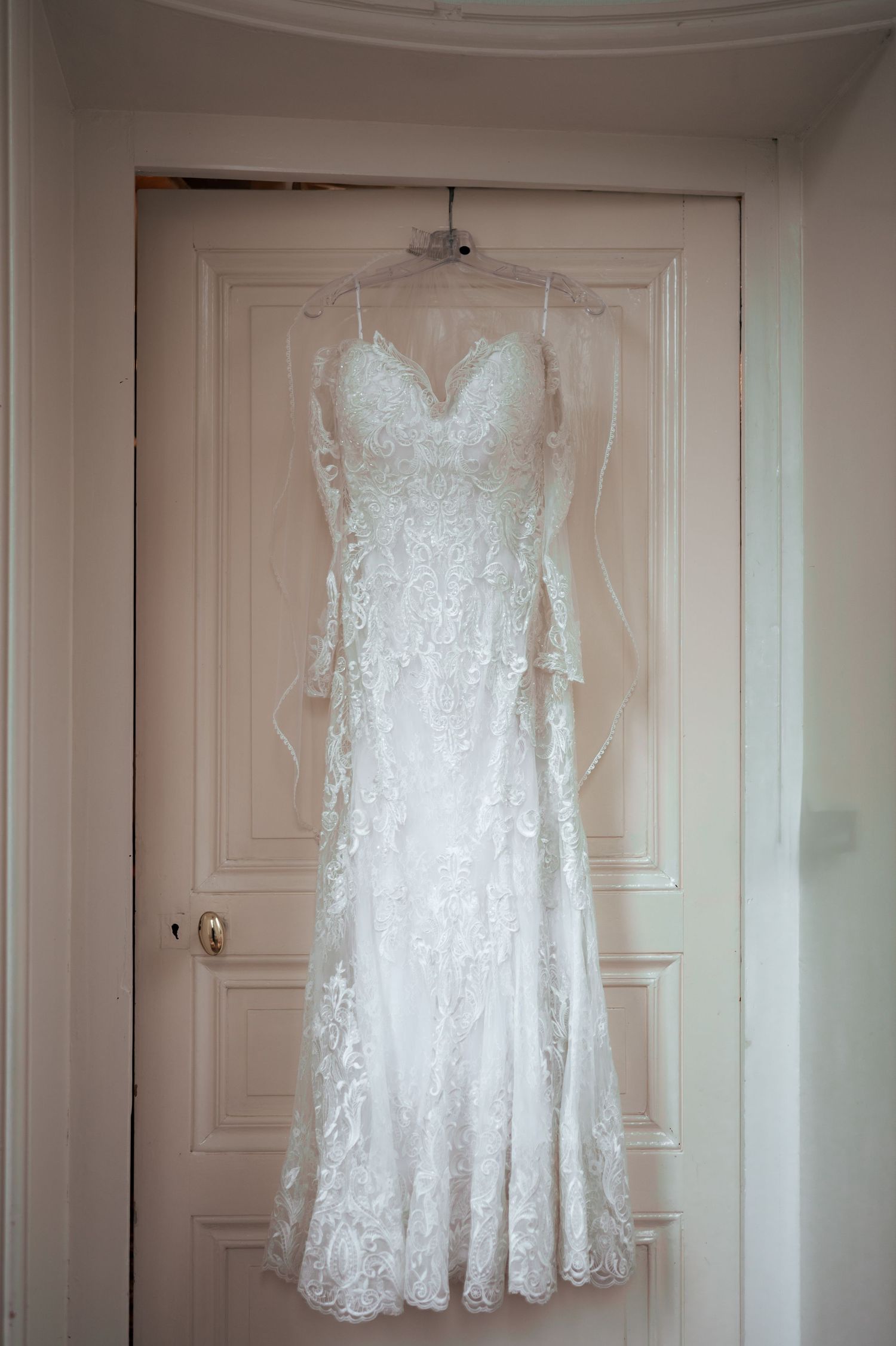 Elegant lace wedding dress with sweetheart neckline hanging on a white door before the ceremony.