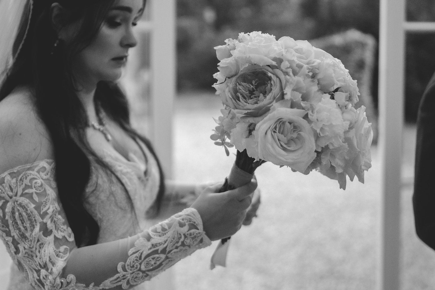 Black and white close-up of bride holding a beautiful bouquet of roses and peonies.