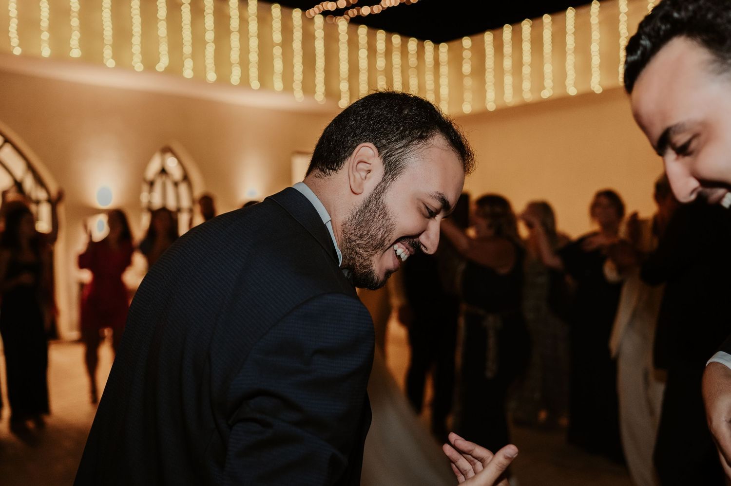 Man in suit laughs joyfully while leaning forward on the wedding reception dance floor.