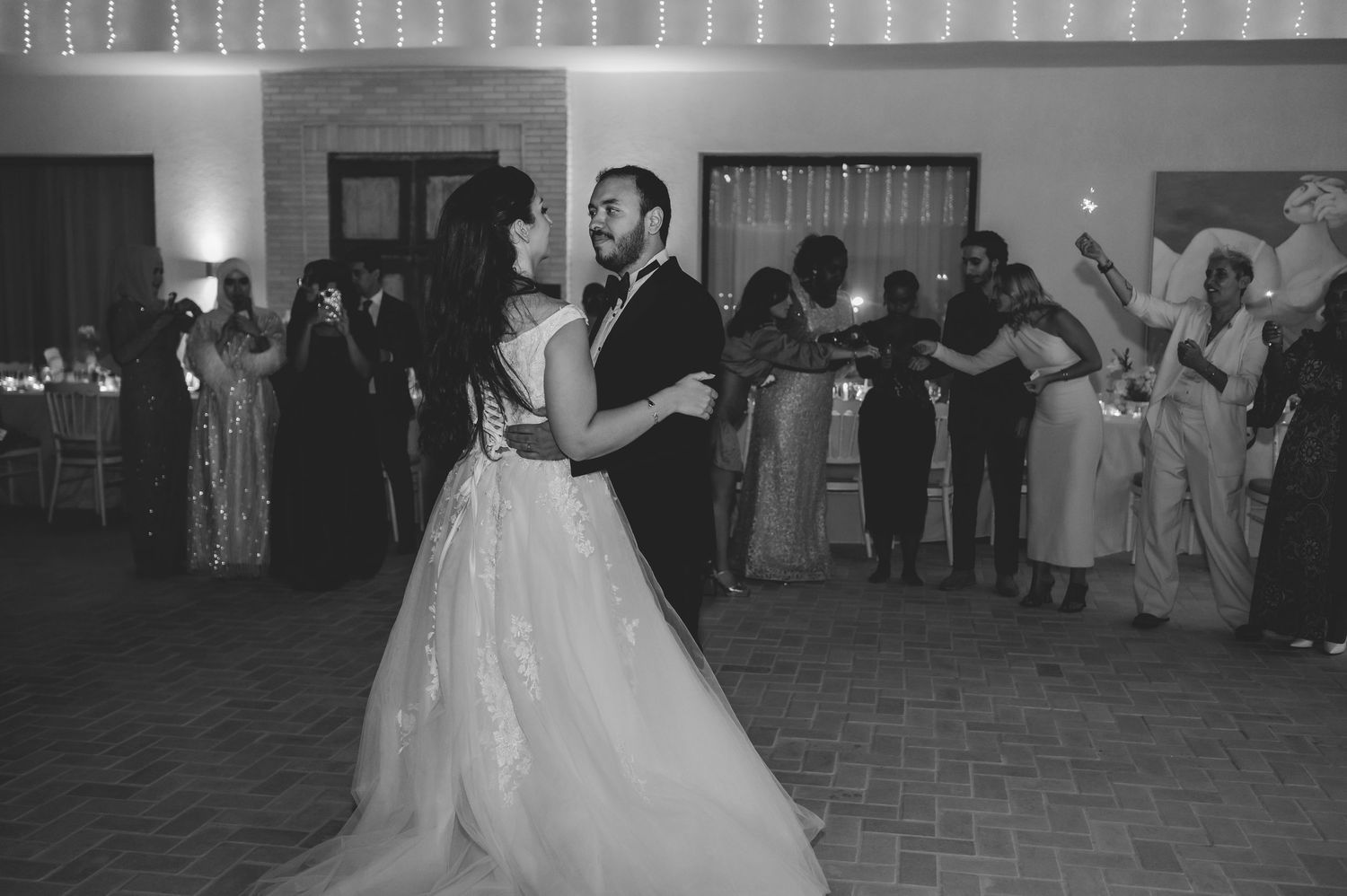 Bride and groom share first dance surrounded by guests holding sparklers in black and white.