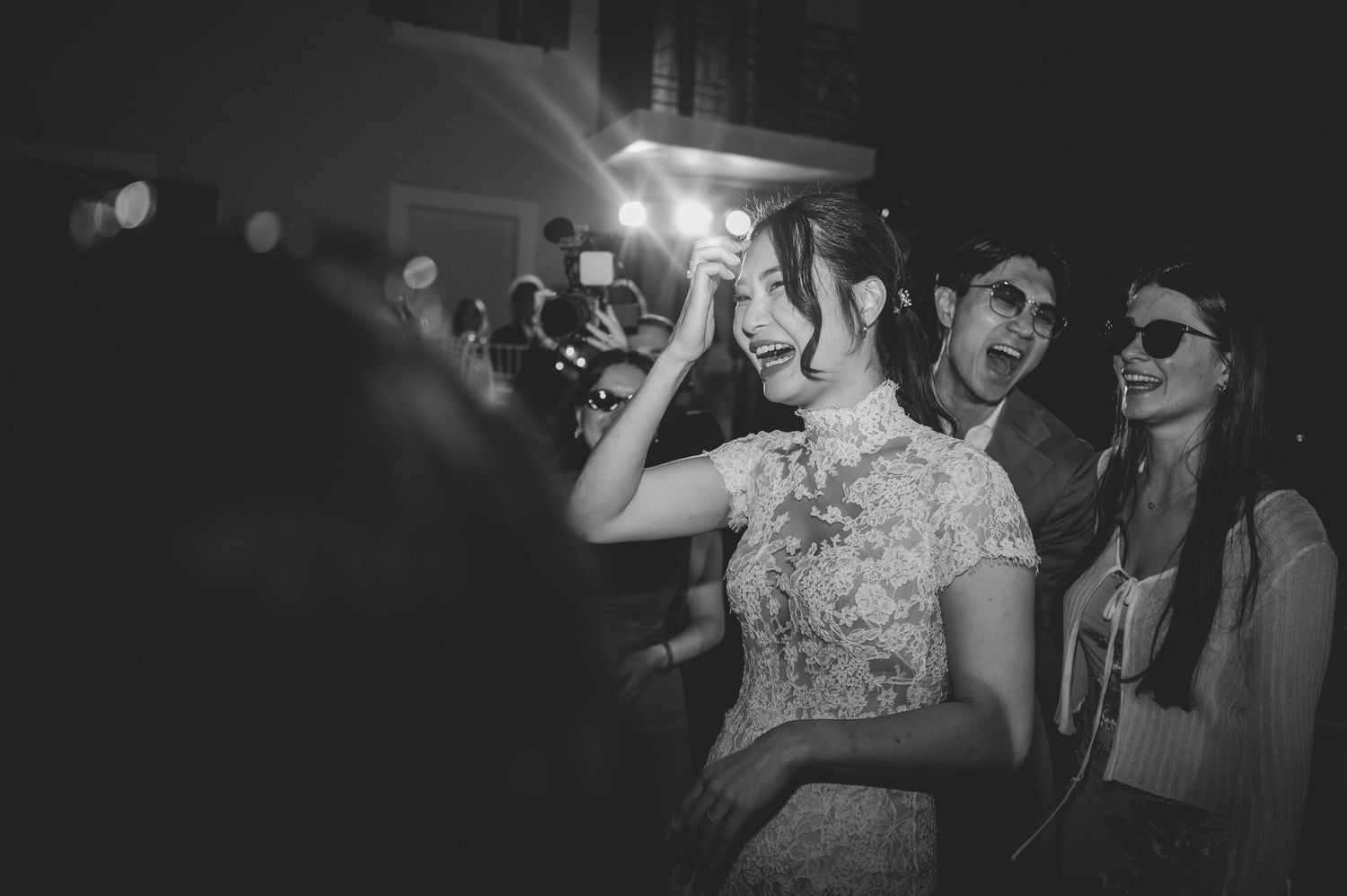 Bride laughing with guests on the dance floor at a wedding reception in black and white.