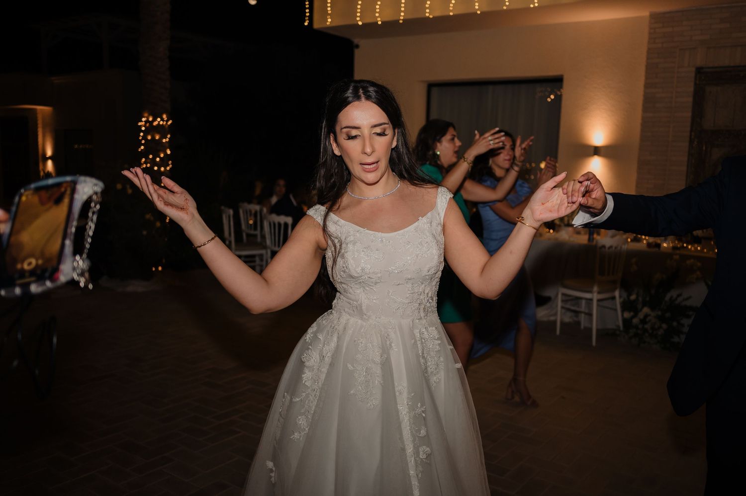 Bride in a white lace wedding gown dancing joyfully with sparklers at her reception.