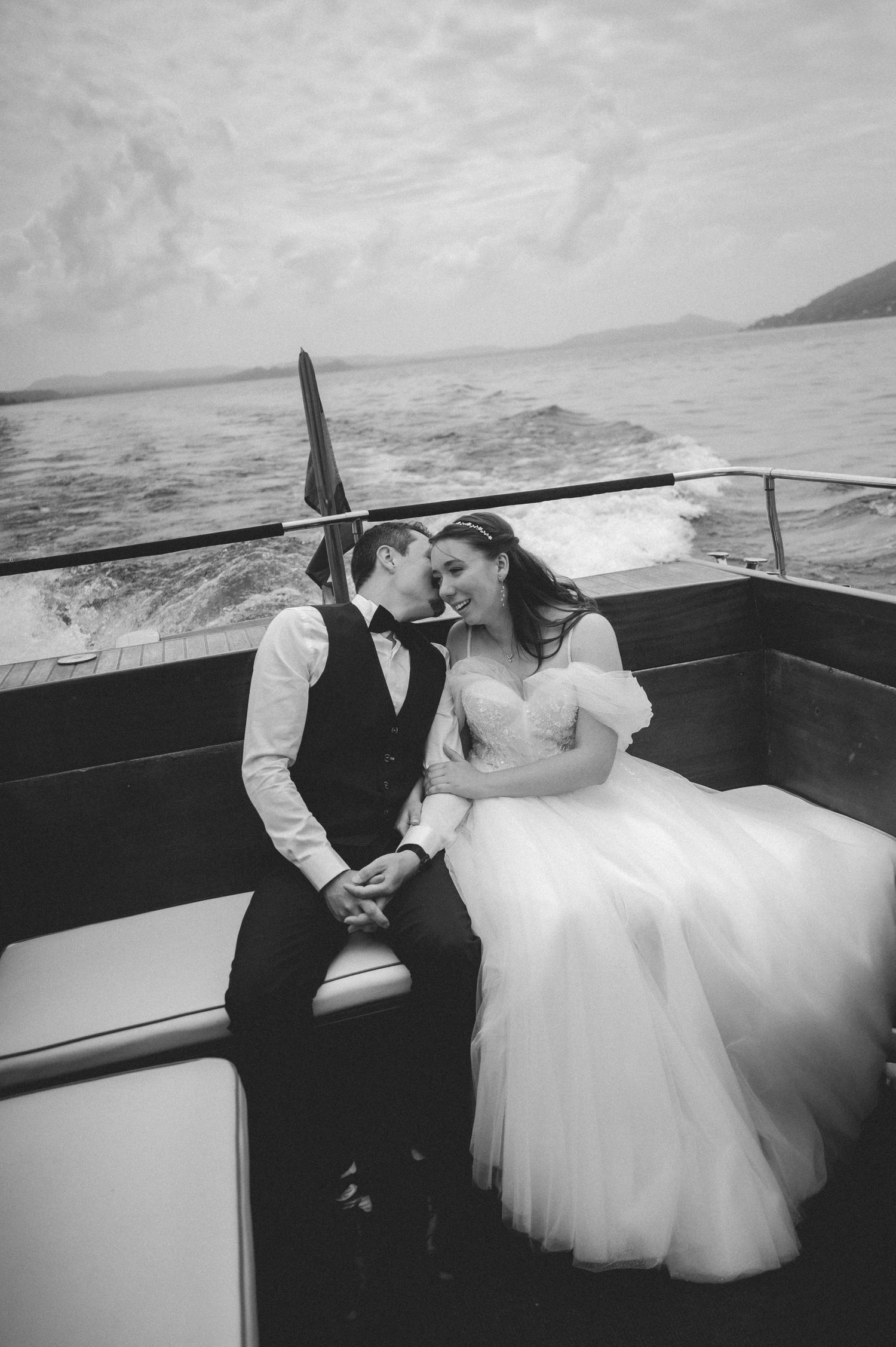 Black and white photo of bride and groom sharing a romantic moment on a boat with ocean views.