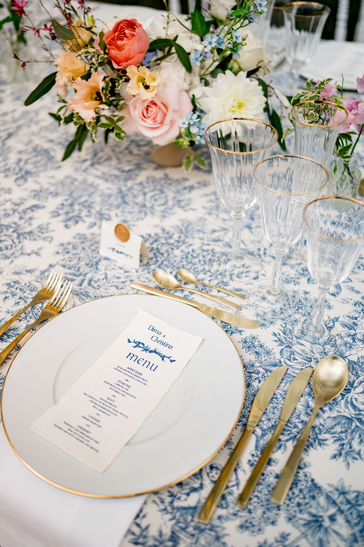 Elegant wedding table setting with blue toile linen, gold flatware, crystal glasses and menu card.