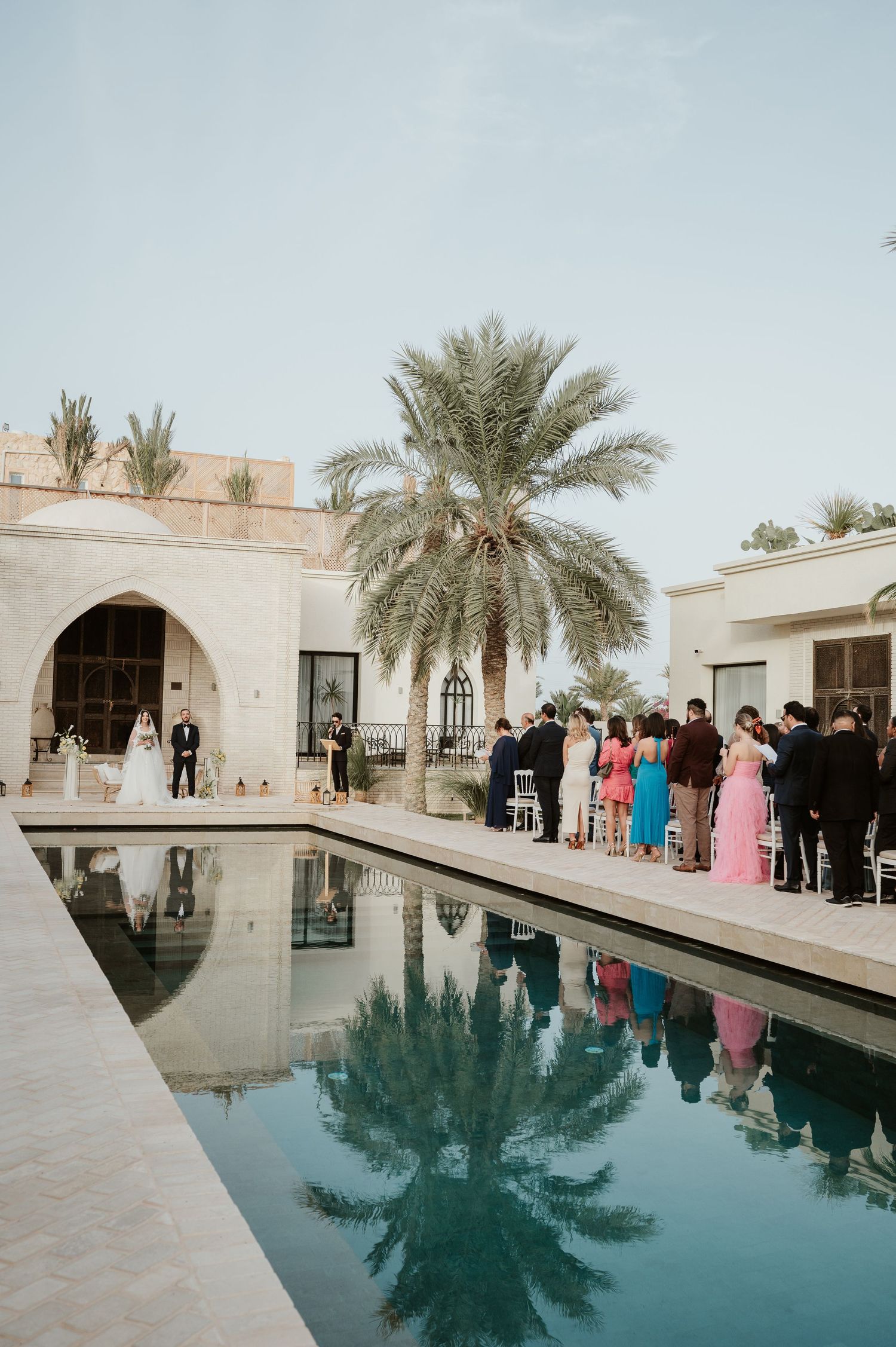 Elegant outdoor wedding ceremony beside a reflective pool with palm trees at a luxury Middle Eastern venue.