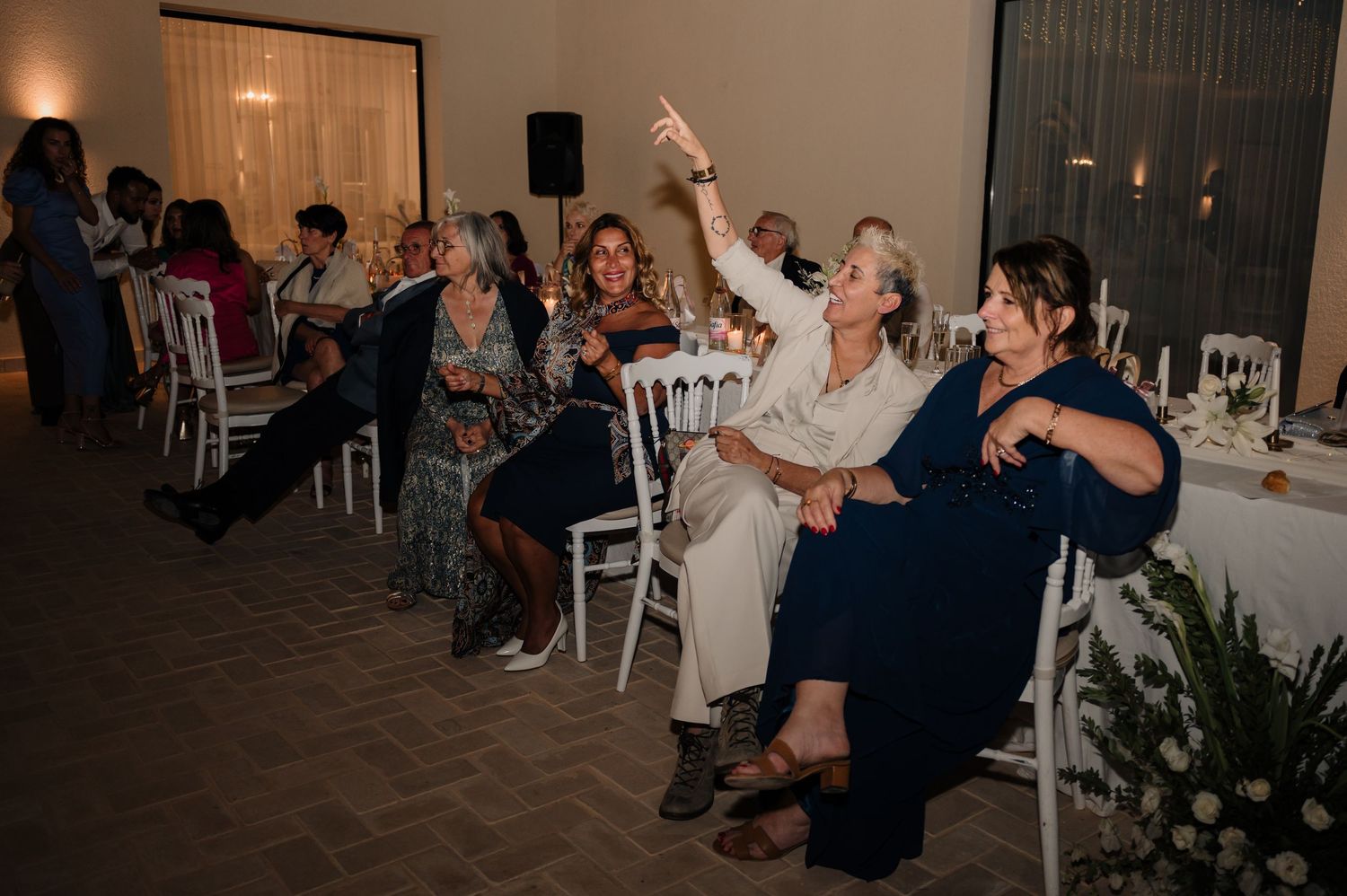 Wedding guests seated at tables raising glasses and taking photos during the reception.