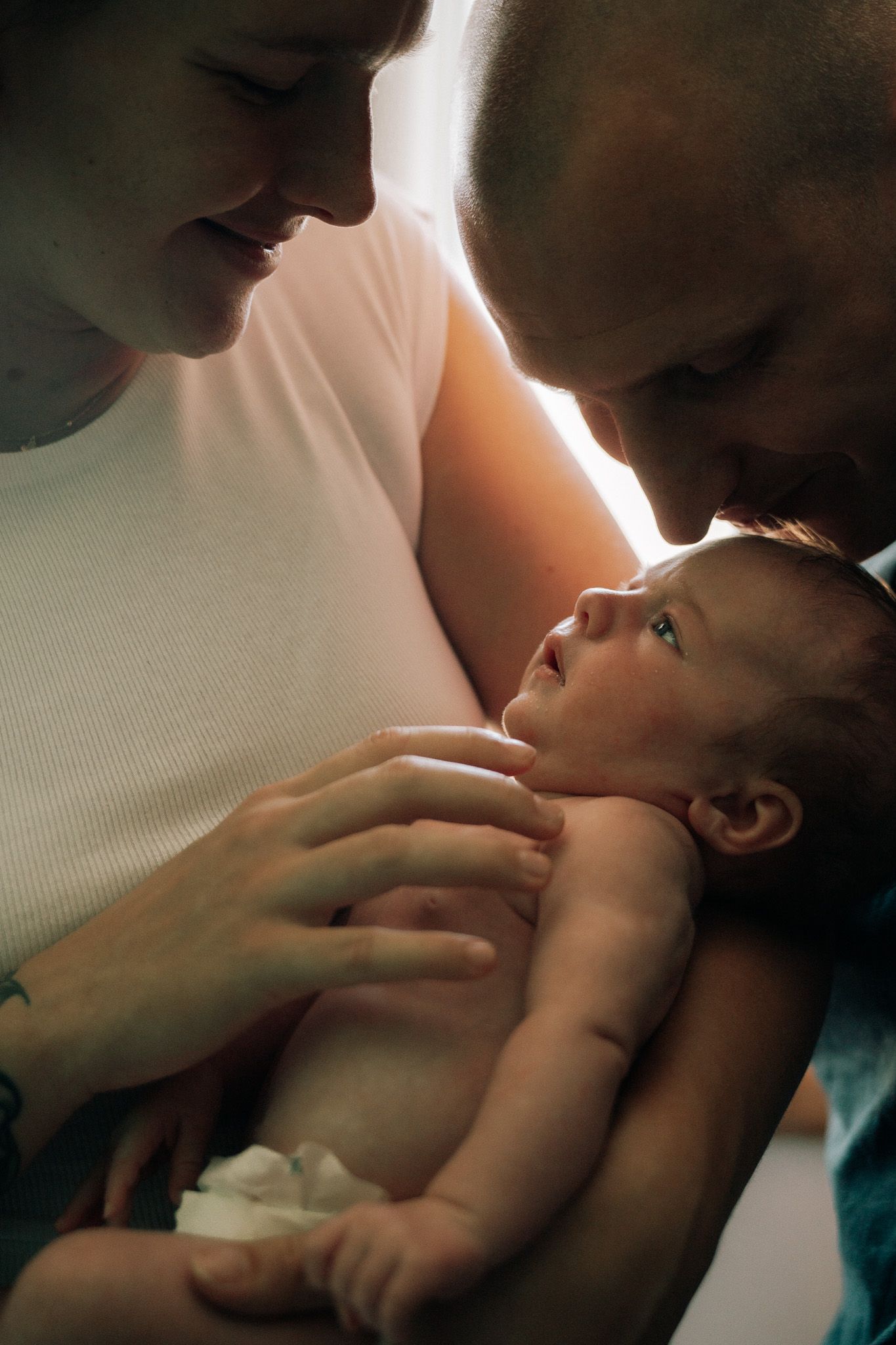 Close-up of new parents lovingly gazing at their newborn baby held in mothers arms.