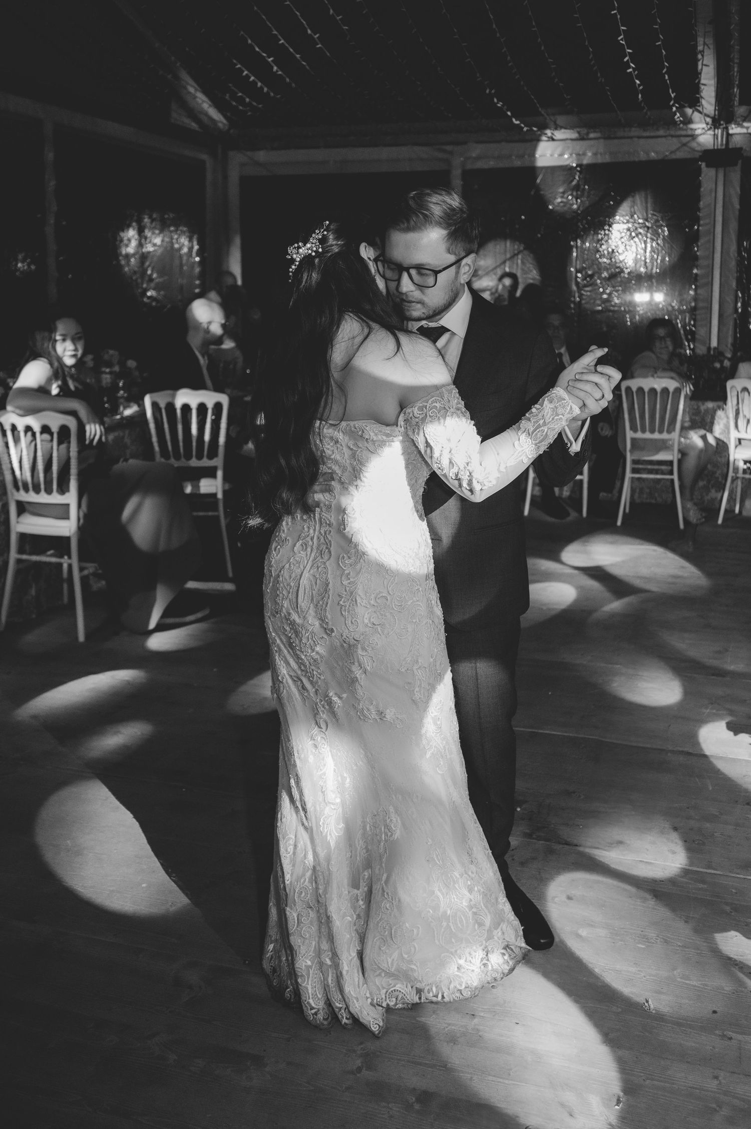 Black and white photo of bride and groom sharing their first dance in a spotlight.