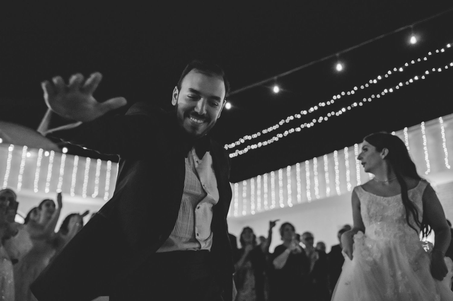 Groom dances energetically with bride at wedding reception in black and white photo.