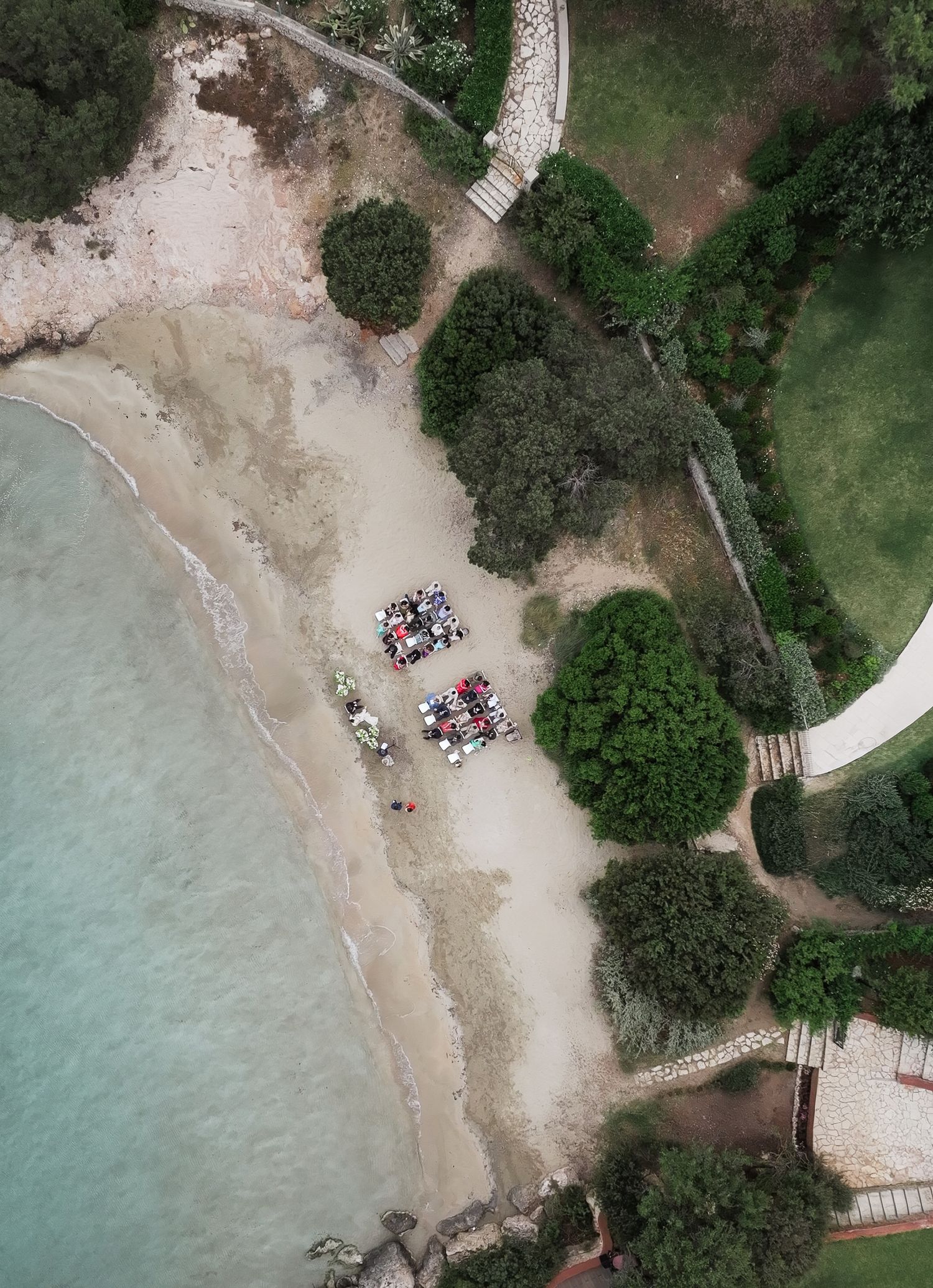 Aerial drone view of intimate beach wedding ceremony surrounded by green coastal landscape.