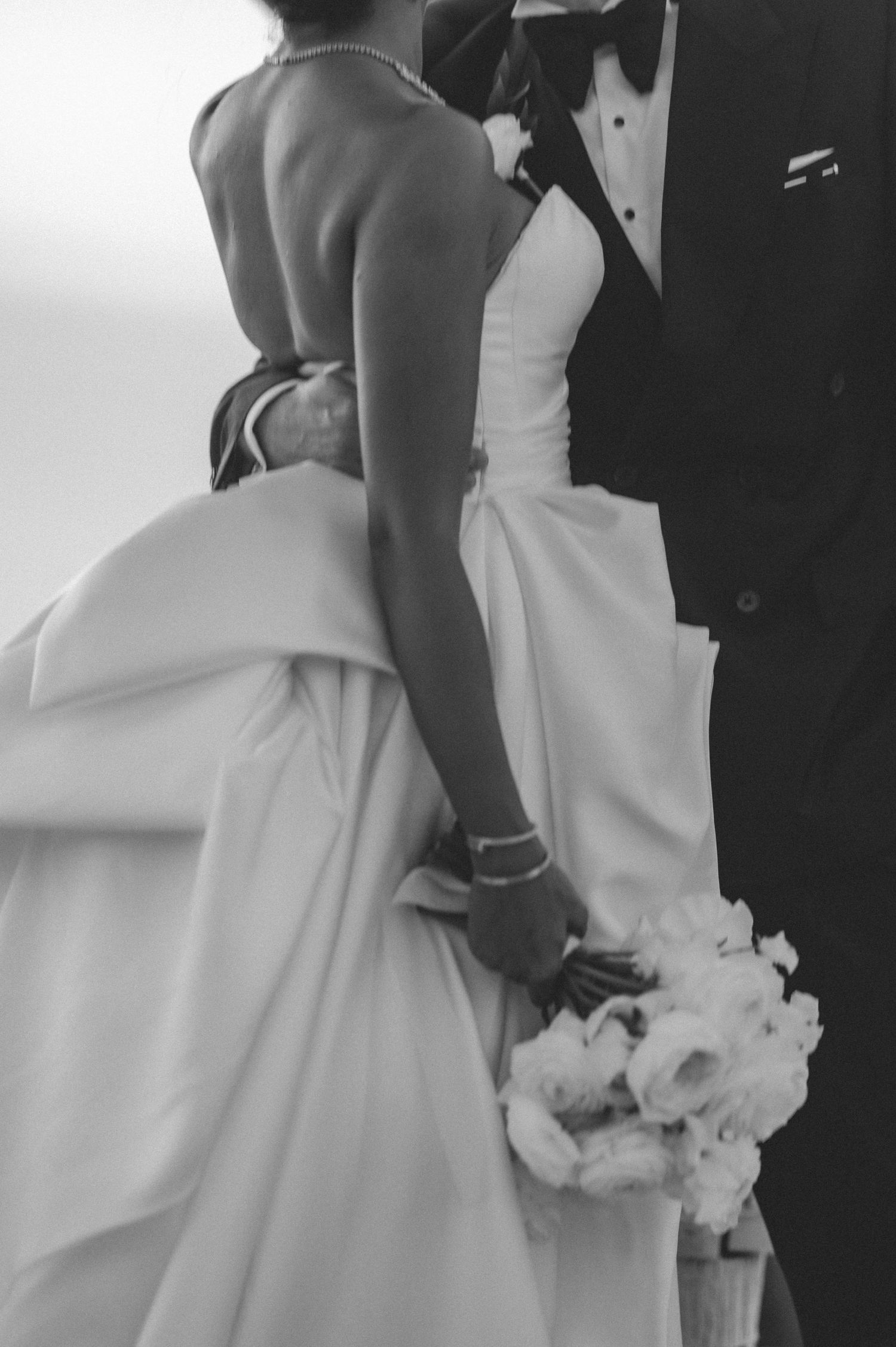 Black and white photo of bride and groom holding hands with white floral bouquet at wedding.