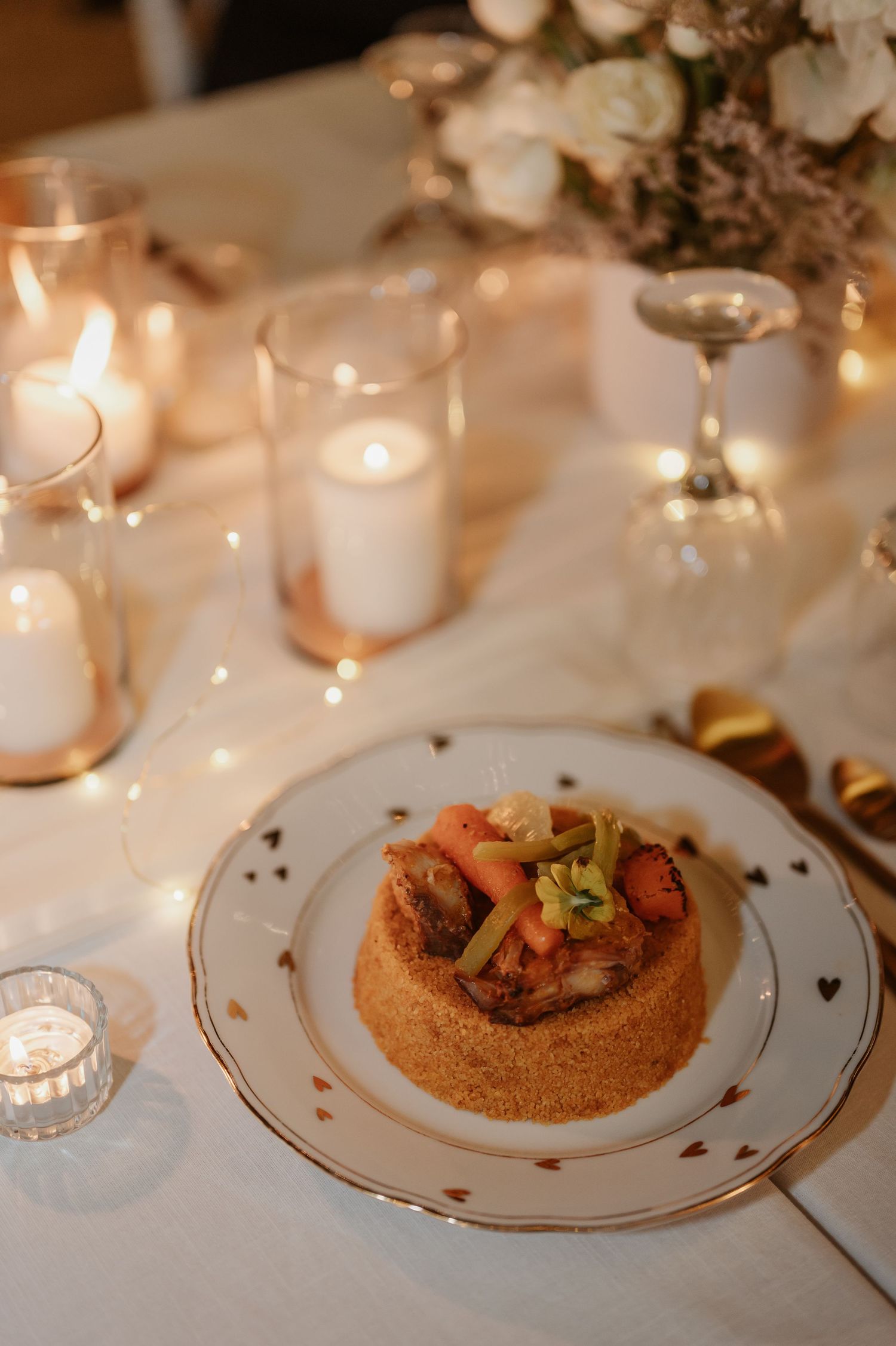 Elegant wedding dinner plate with stuffed pastry and vegetable topping surrounded by candles and white flowers.
