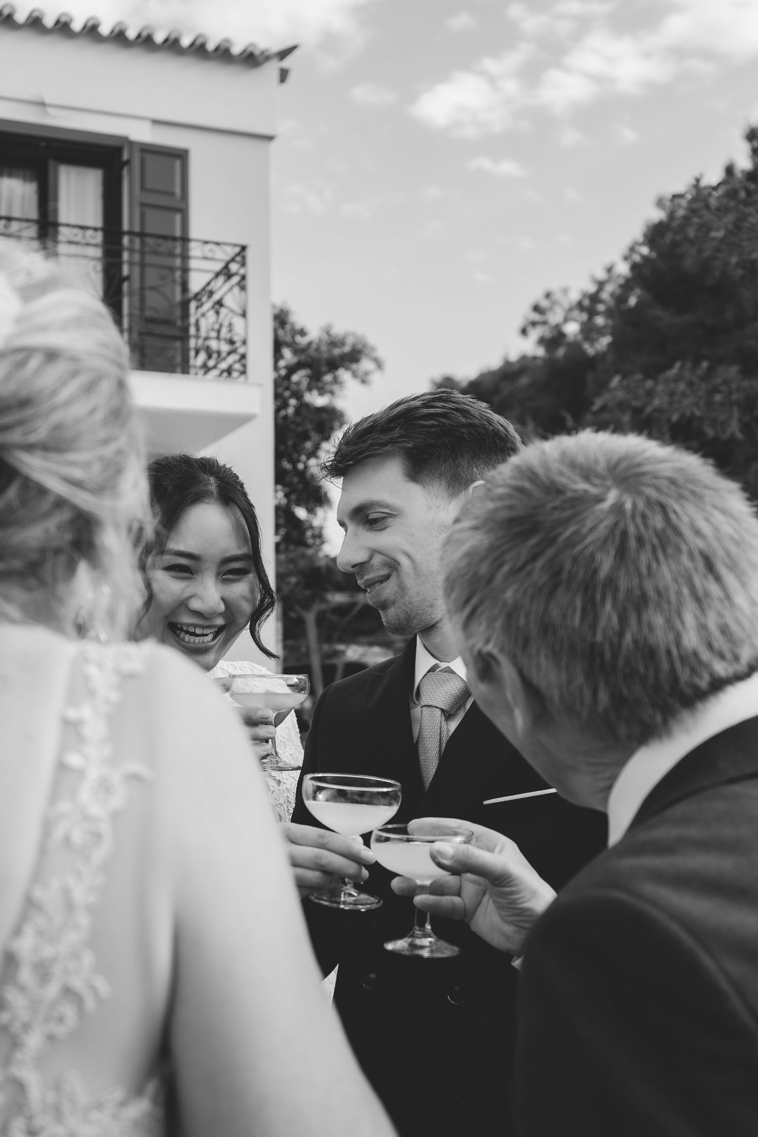 Black and white photo of wedding guests toasting with cocktails outdoors, smiling bride and groom celebrating.