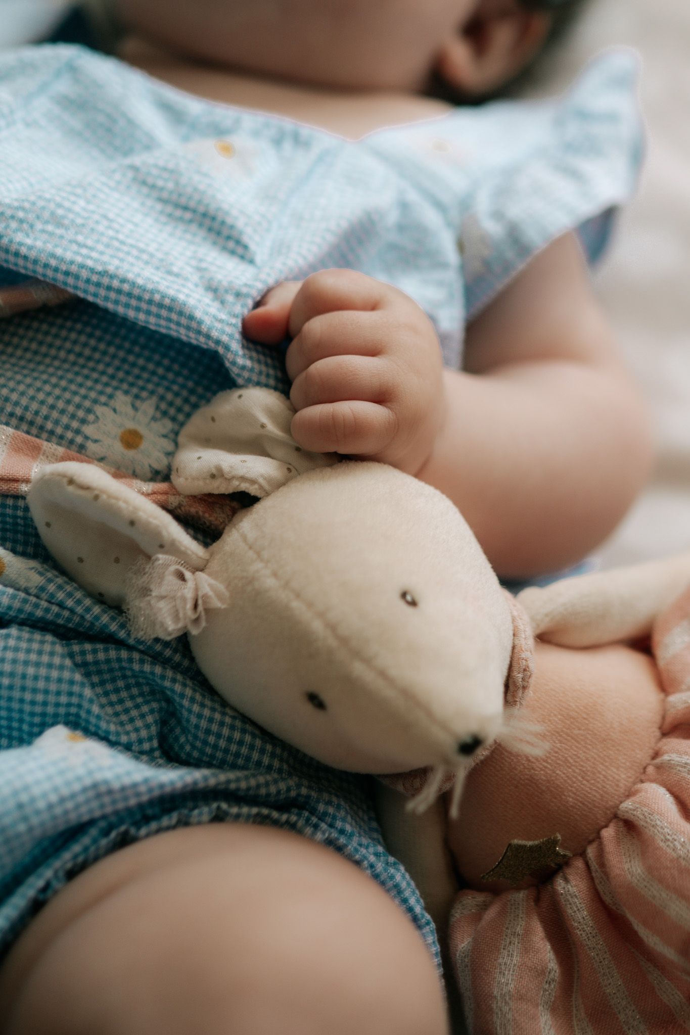 Close-up of a sleeping baby in a blue floral outfit clutching a soft stuffed bunny toy.