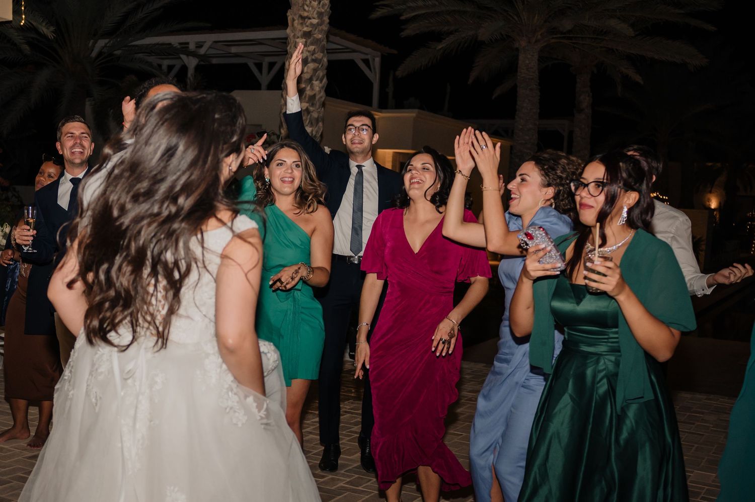 Wedding guests dance and celebrate outdoors with bride in white gown at evening reception.