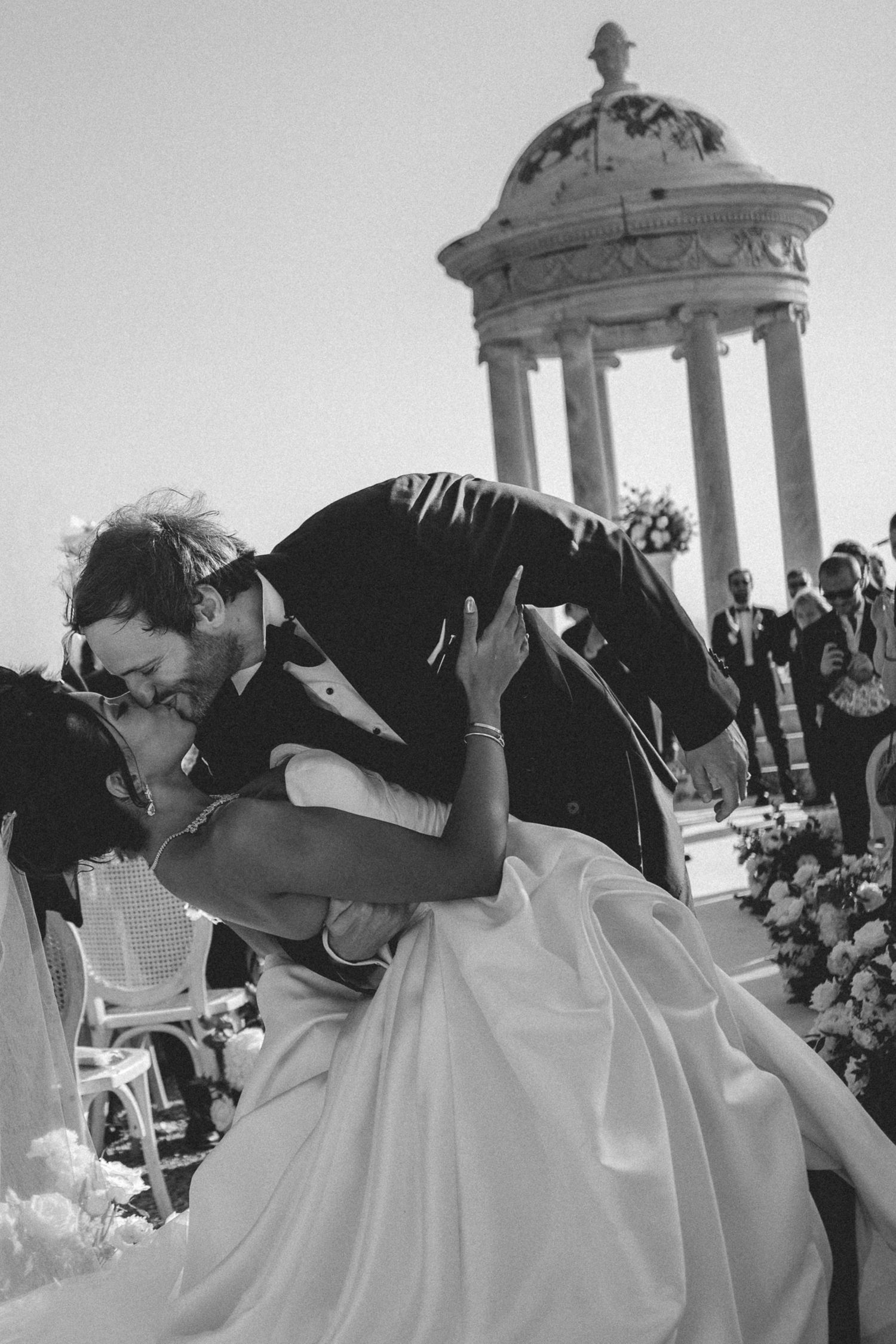 Groom dramatically dips and kisses bride in black and white photo with classical rotunda backdrop.