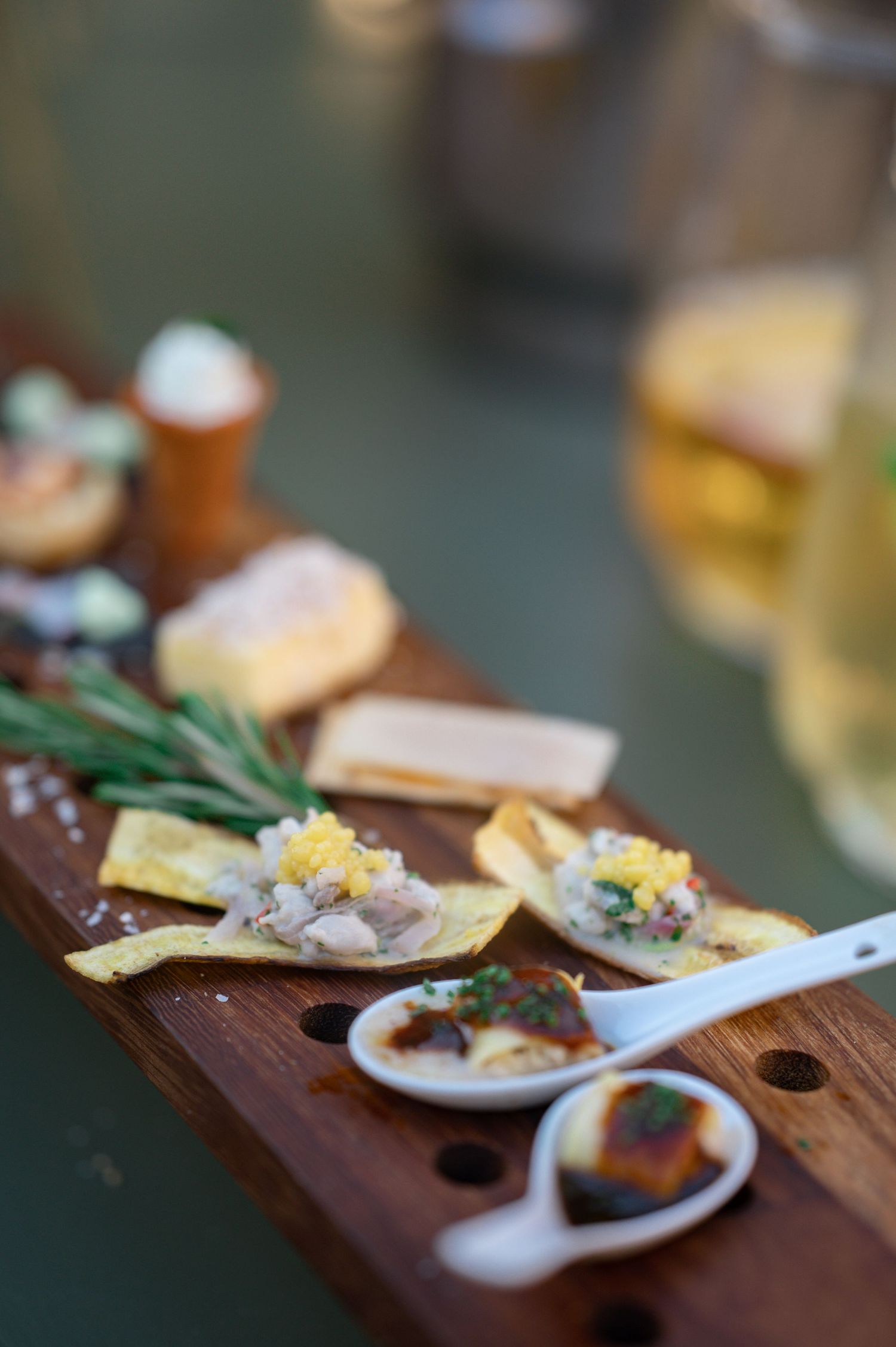 Close-up of gourmet wedding canapés and appetizers arranged on a wooden serving board with rosemary garnish.