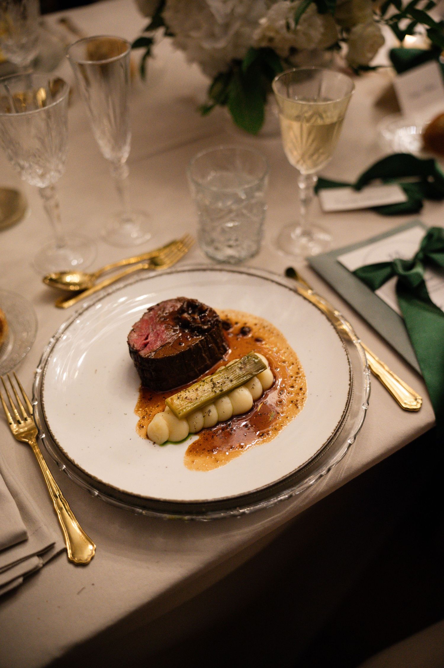 Elegant wedding dinner plate featuring a perfectly cooked beef filet with asparagus and rich sauce on silver charger.