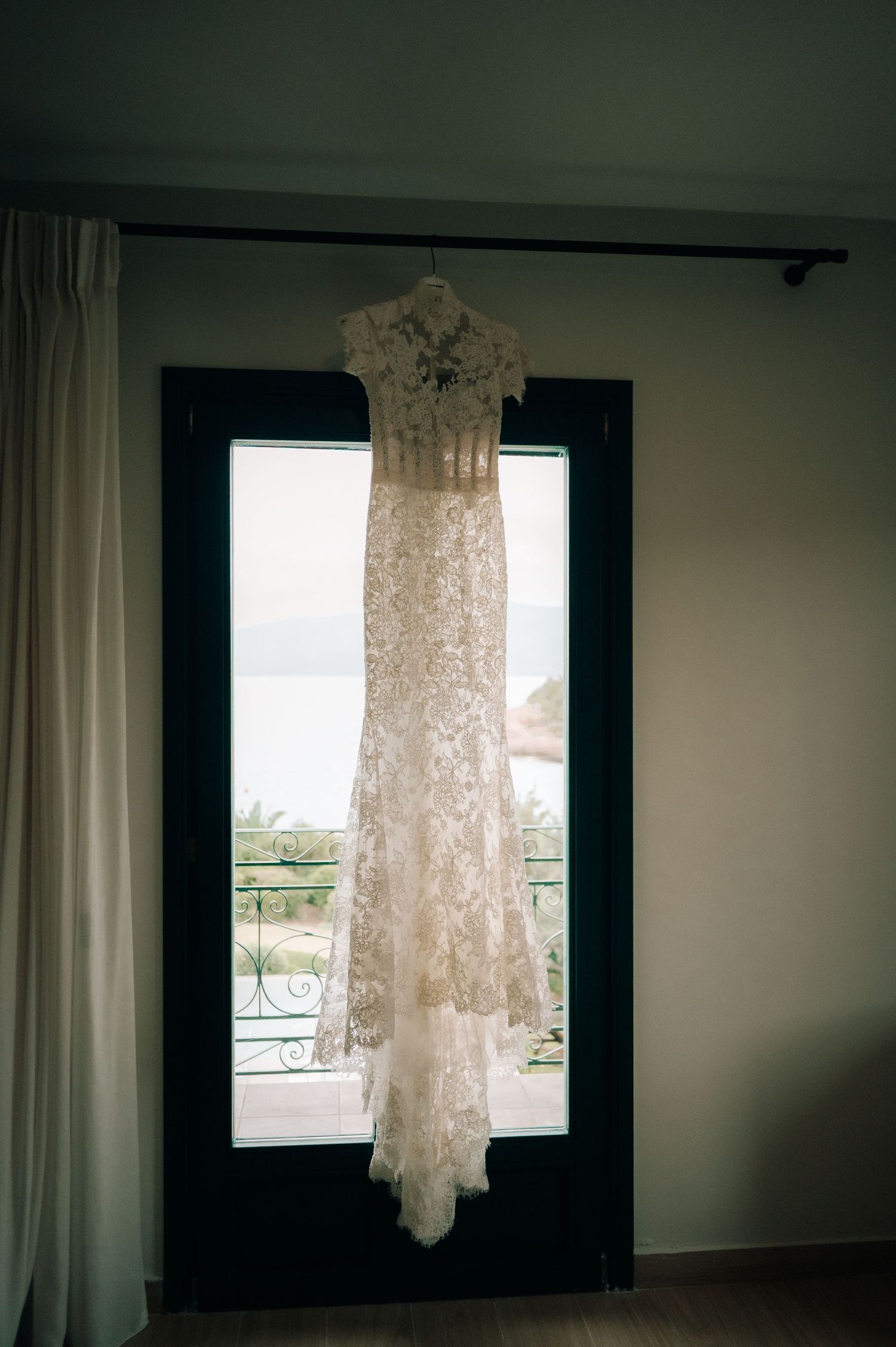 Elegant lace wedding dress with cap sleeves and button back detail hanging on a dark door frame.
