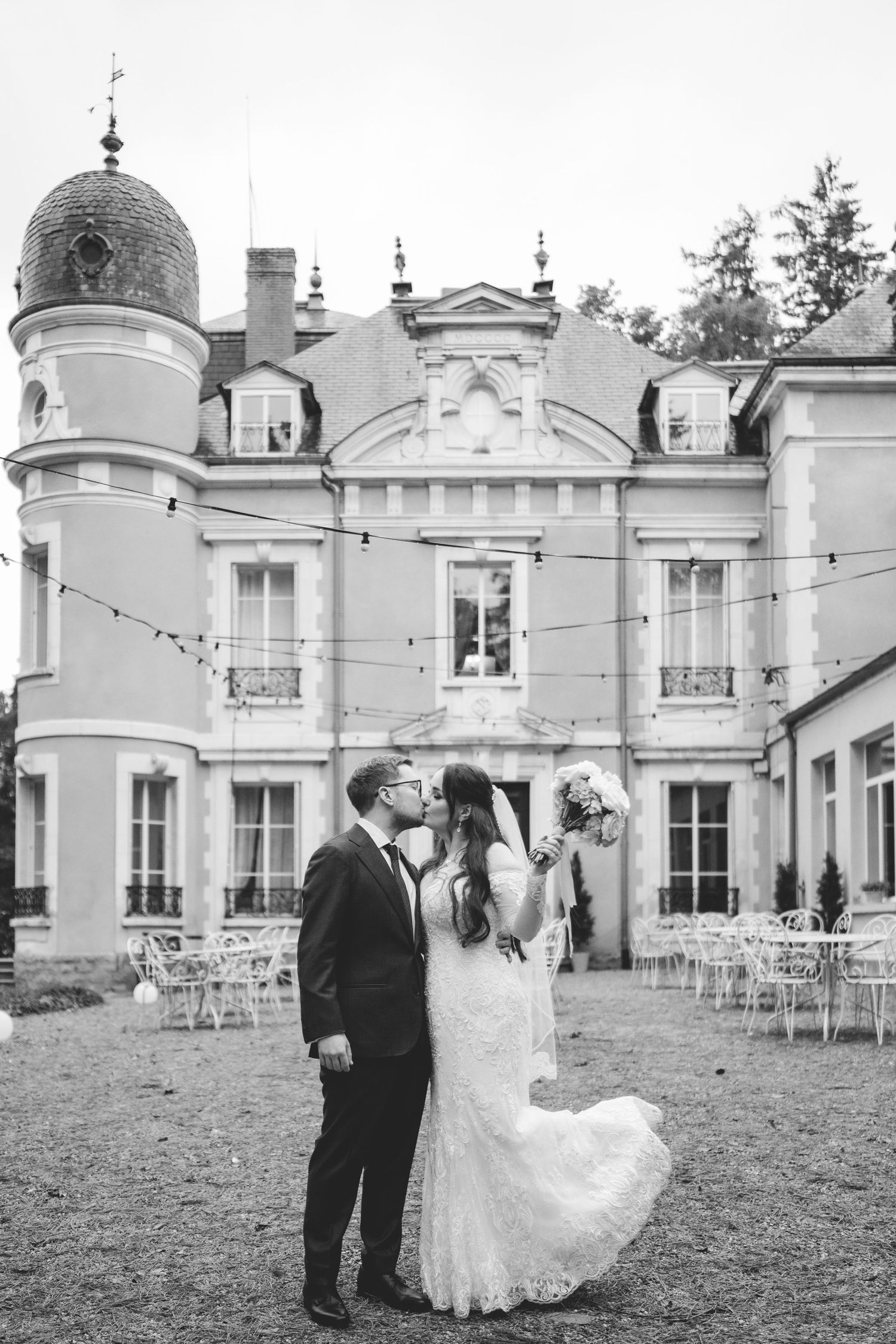 Black and white photo of newlyweds kissing before a grand French chateau wedding venue.