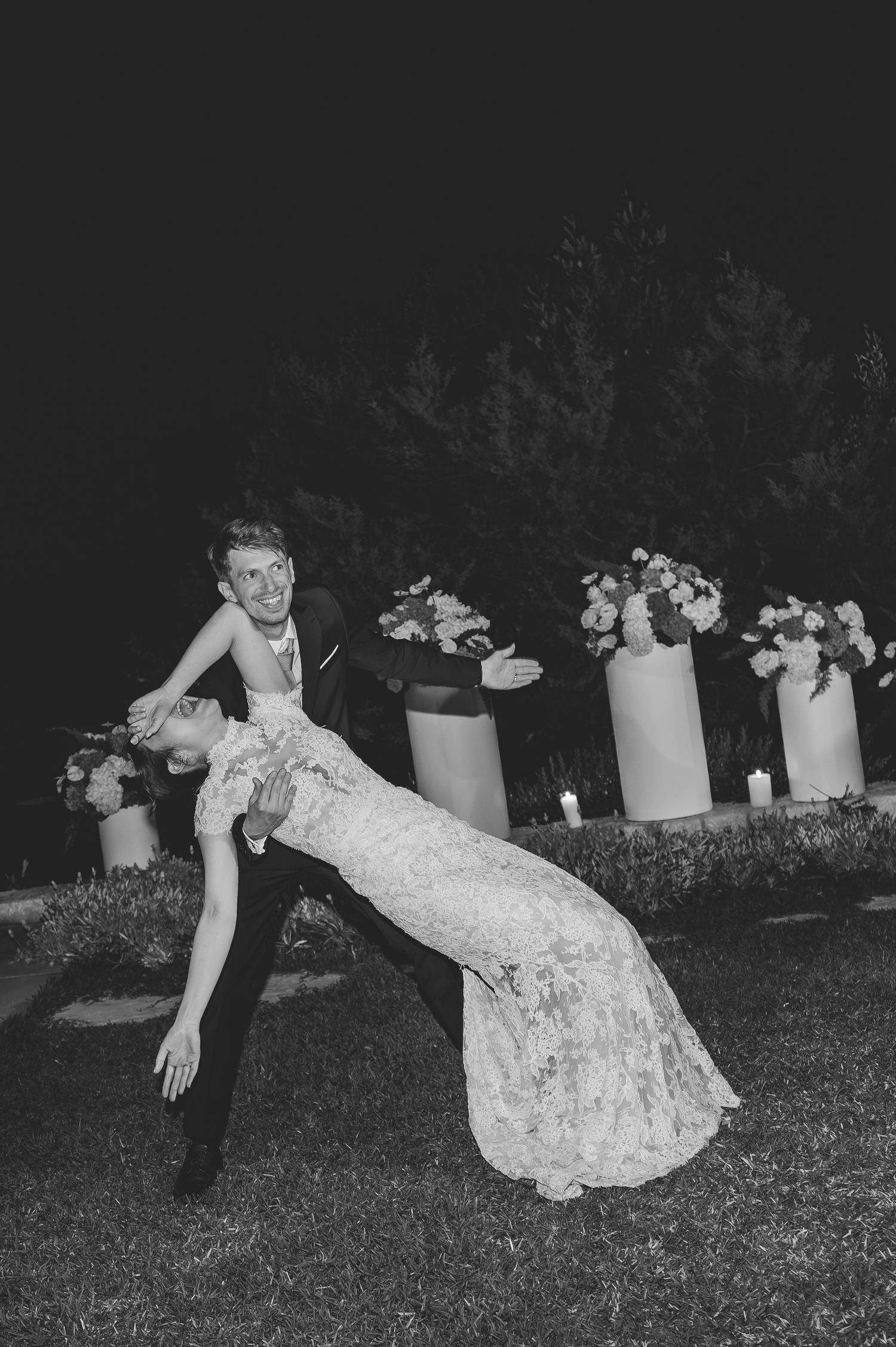Groom dipping bride dramatically during first dance at outdoor wedding reception in black and white.