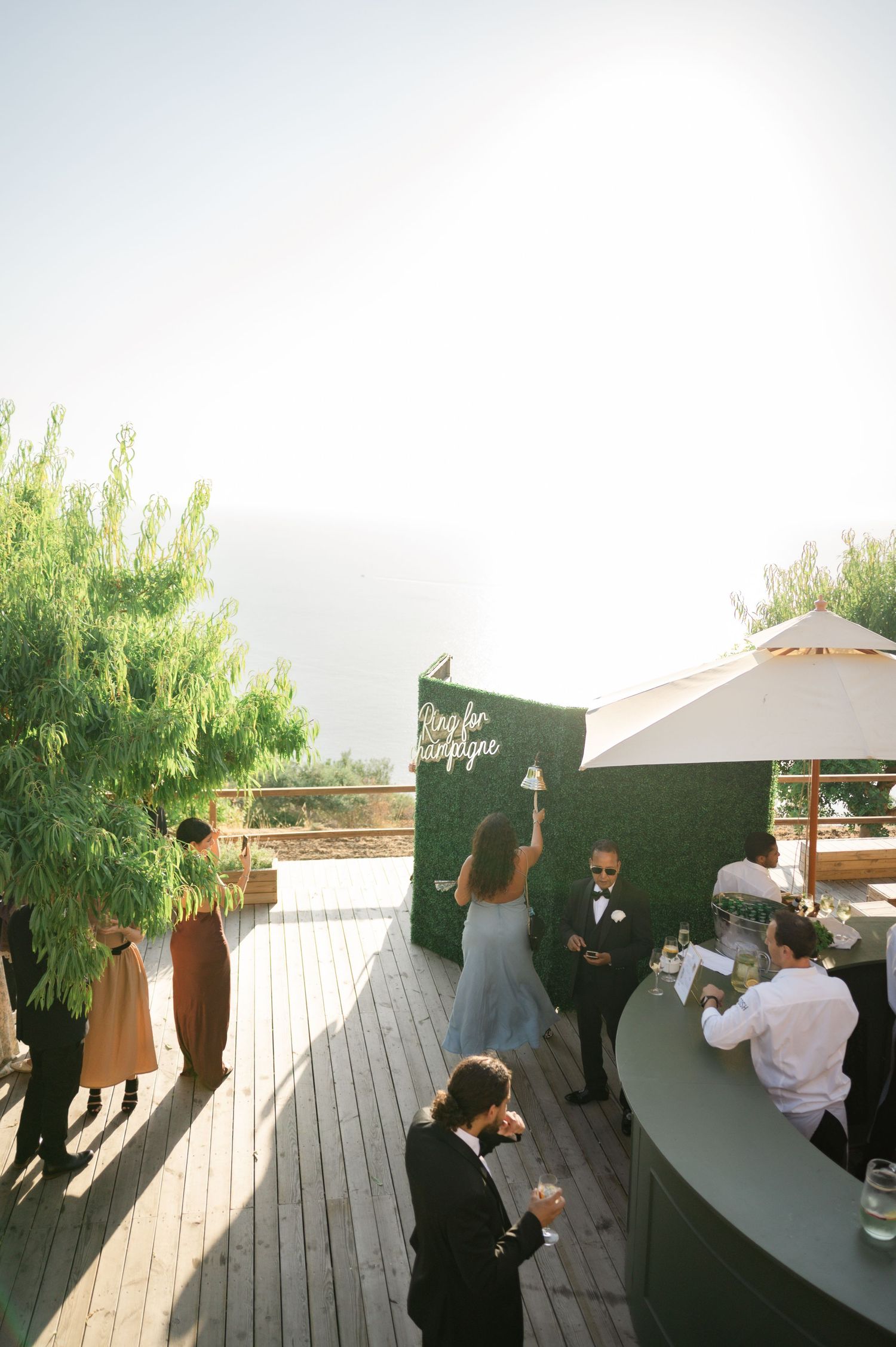 Bride and groom celebrate at outdoor wedding reception bar with Ring for Champagne neon sign.