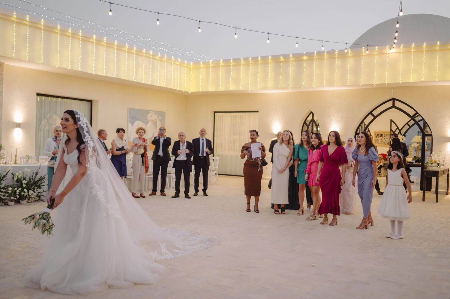 Bride in ball gown preparing to toss bouquet to guests at elegant wedding reception.