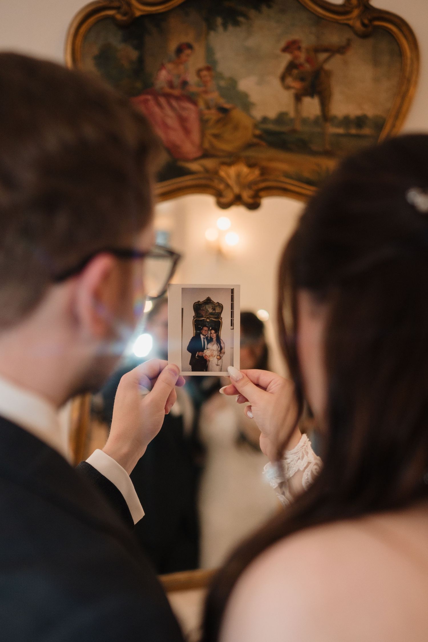 Couple examining Polaroid wedding photo in front of ornate gilded mirror at reception.