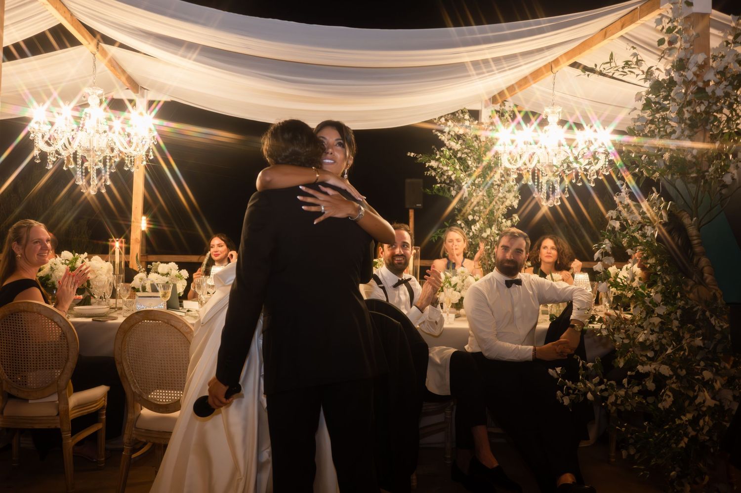 Romantic first dance moment as bride and groom embrace under glittering chandeliers at evening wedding reception.
