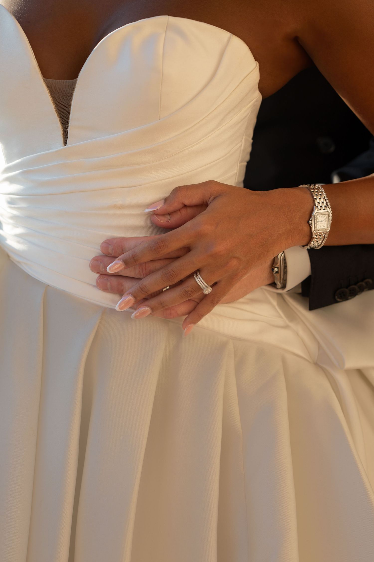 Close-up of couple's hands embracing bride's white strapless gown with wedding rings visible.