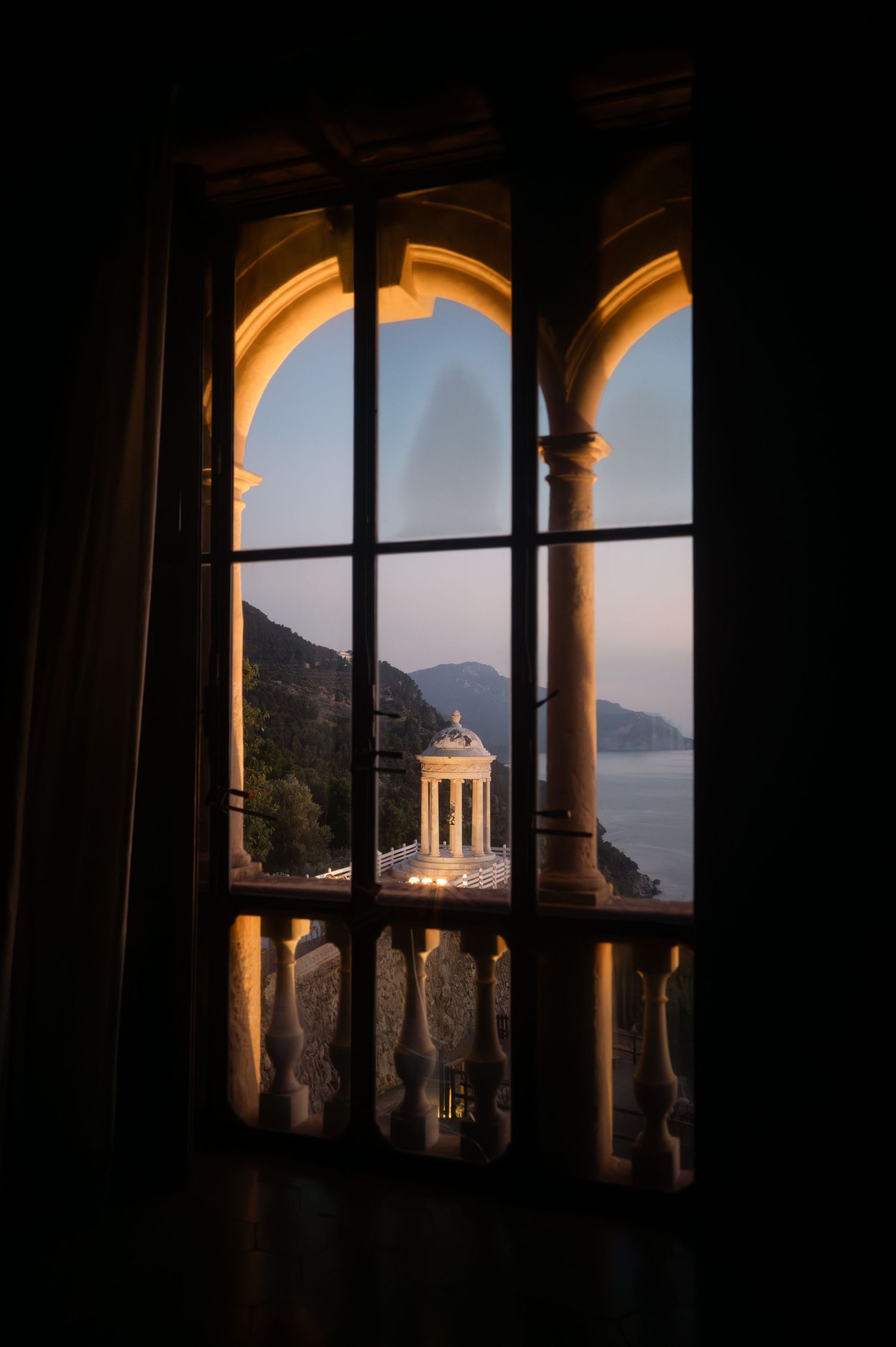 Breathtaking view of a Mediterranean rotunda and sea through an arched stone window at golden hour.