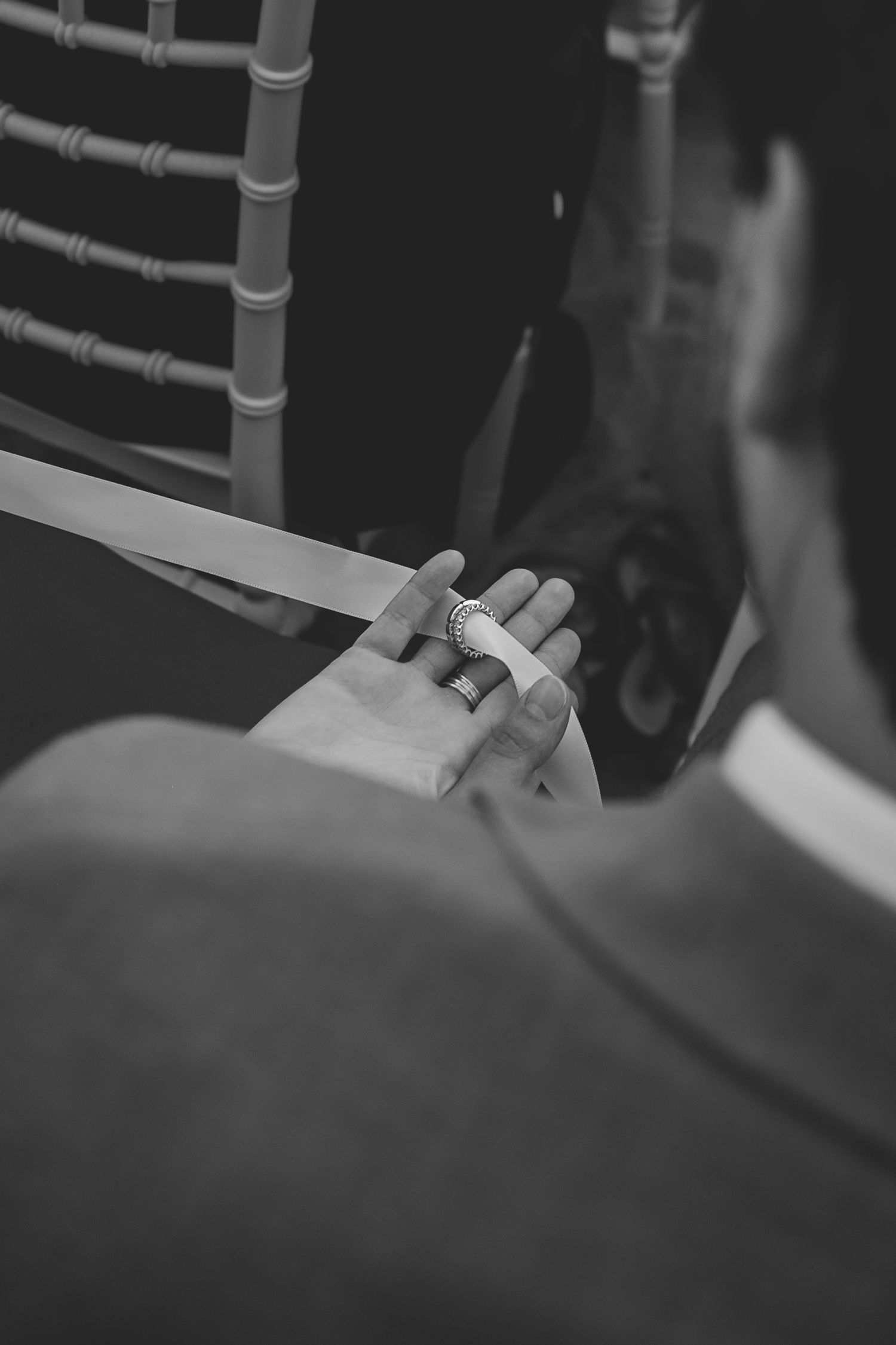 Black and white close-up of bride's hand holding ribbon with elegant ring during wedding ceremony.