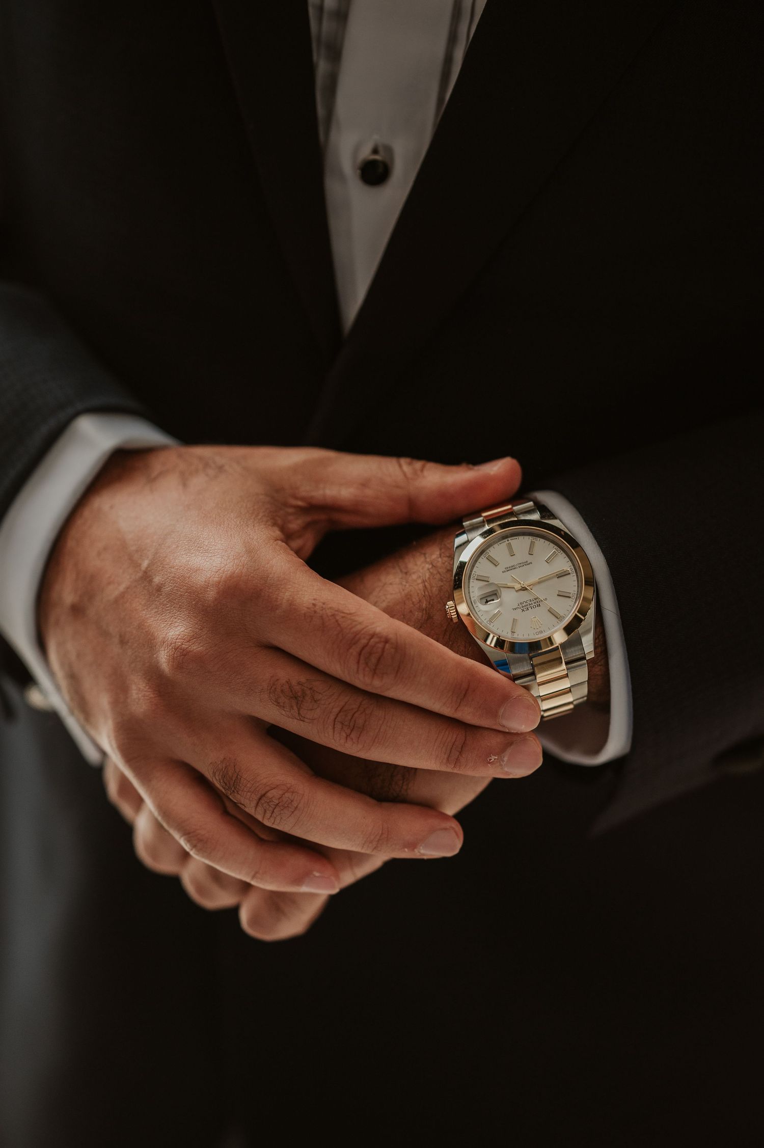 Close-up of groom adjusting gold and silver luxury watch on wrist wearing black tuxedo.