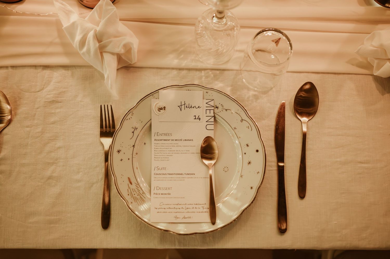 Elegant wedding place setting with gold cutlery, decorative plate, and printed menu card.