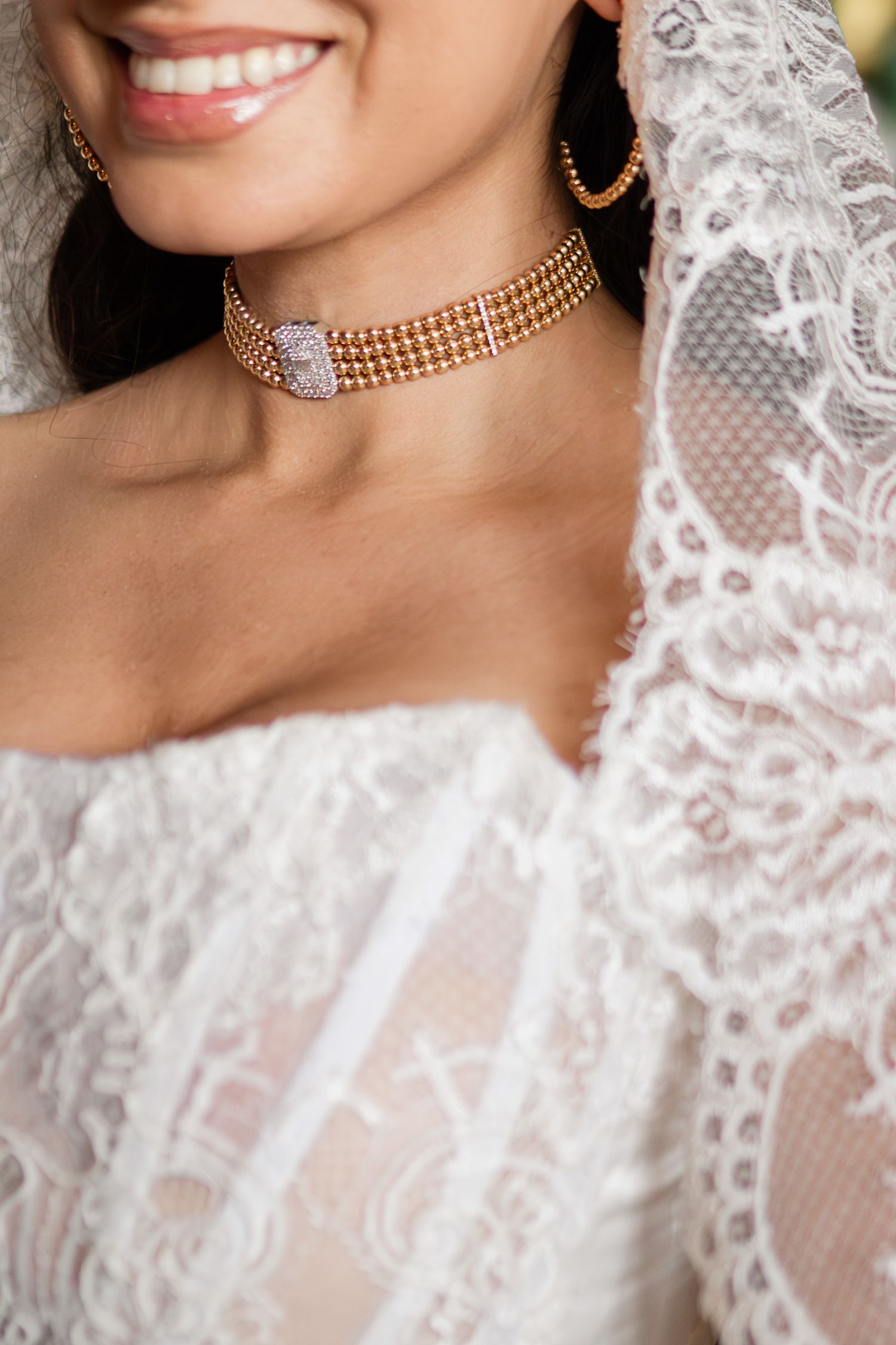 Close-up of bride wearing gold multi-strand choker necklace with diamond clasp and lace wedding dress.
