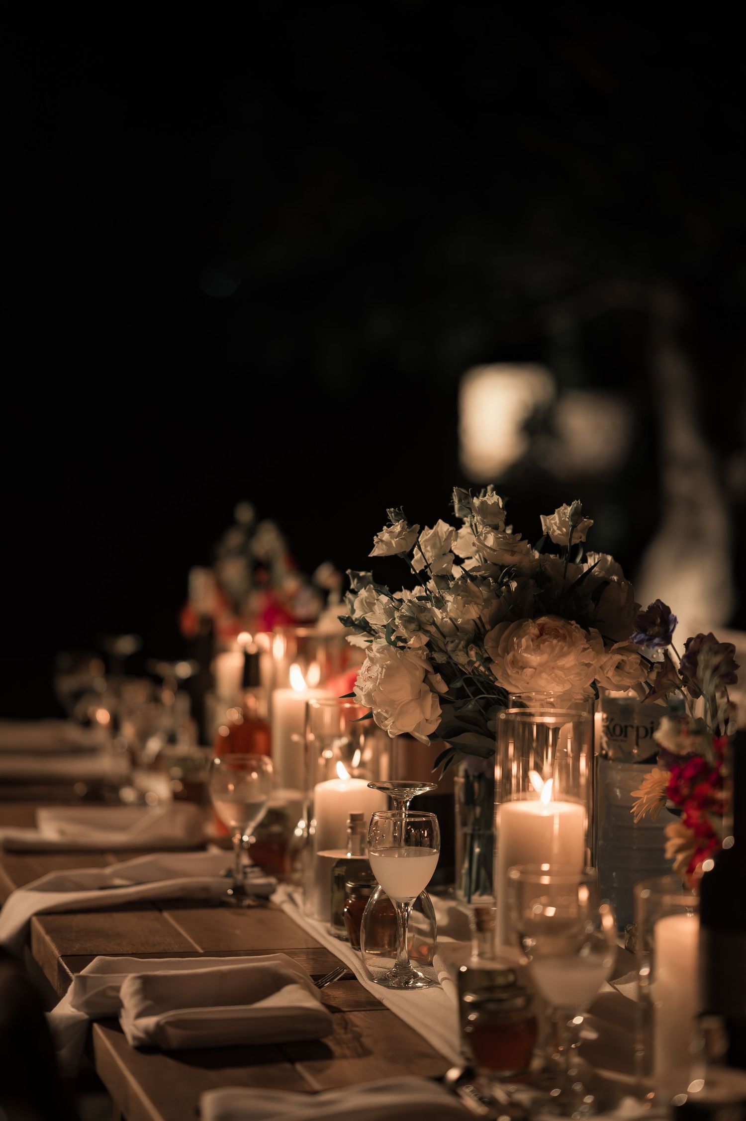 Elegant wedding table setting with white roses, candles, and glassware glowing in the dark night.