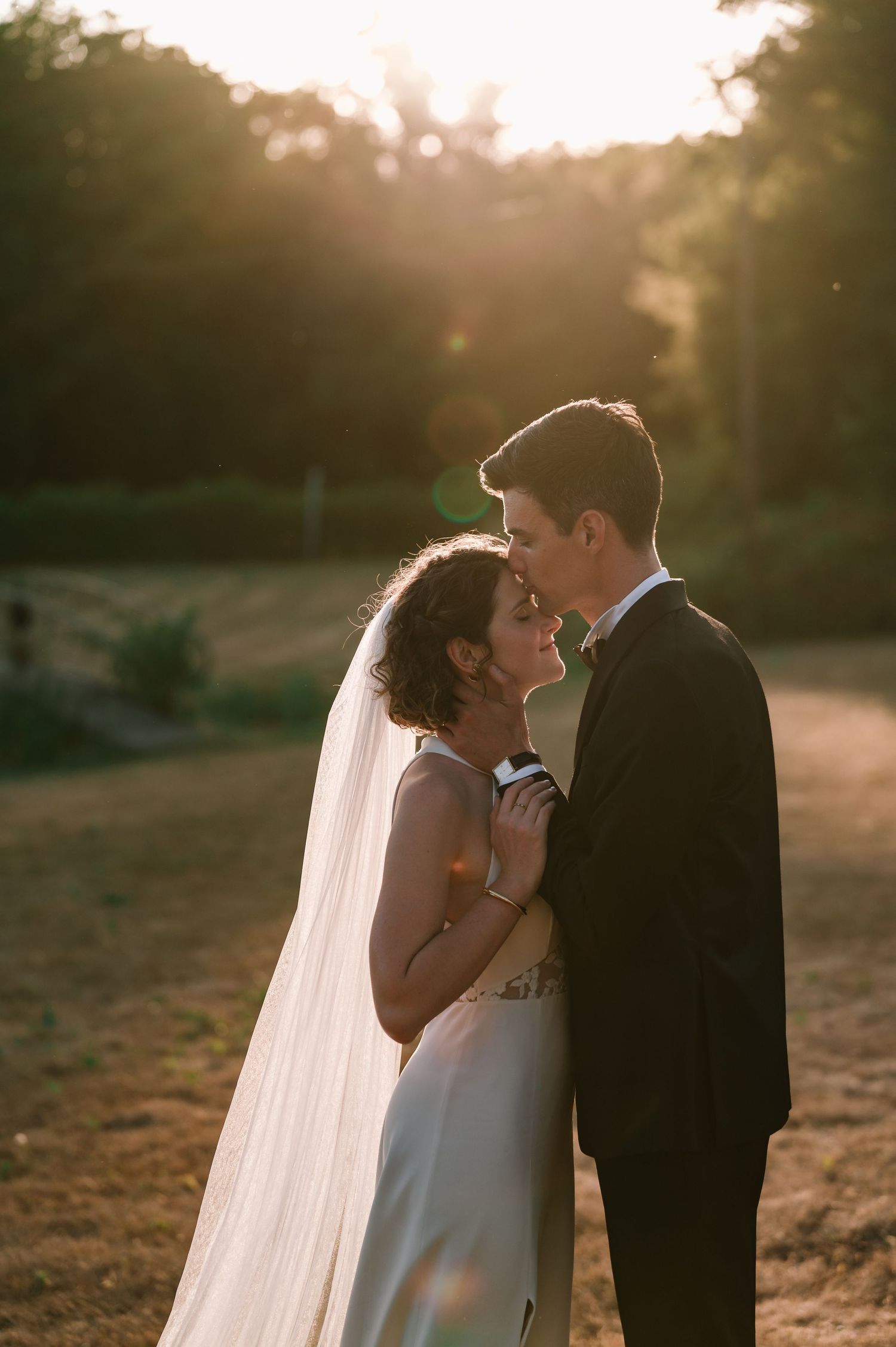 Bride and groom share an intimate moment bathed in warm golden sunset light outdoors.