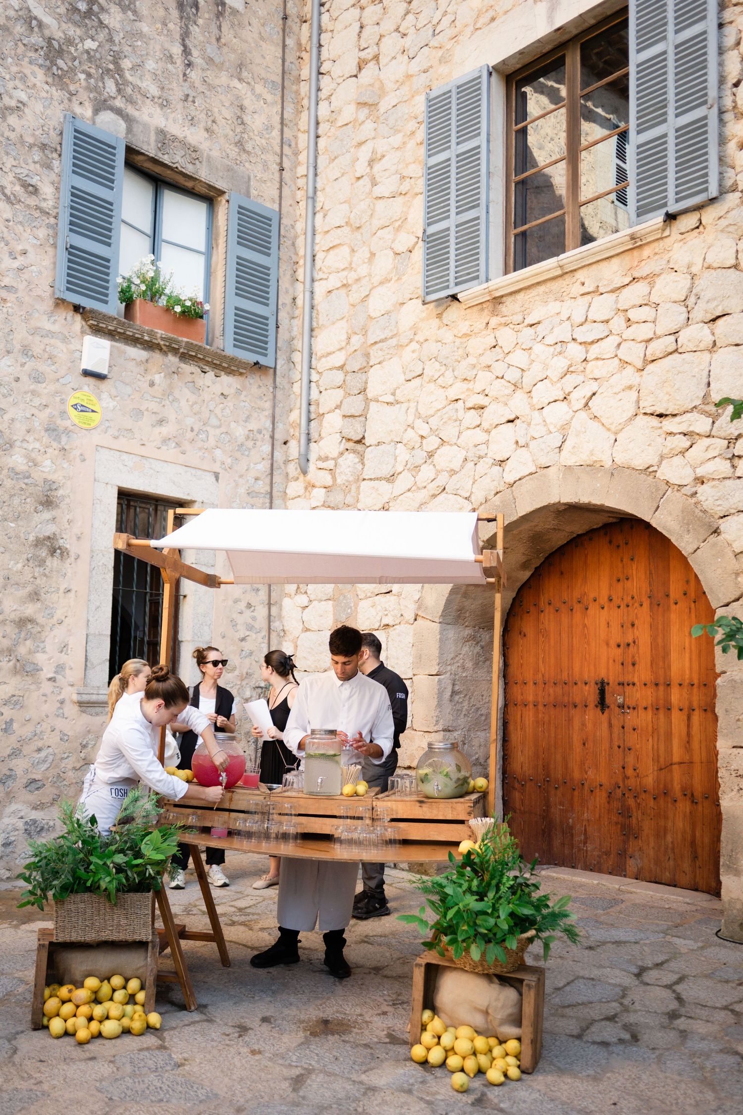 Wedding guests gathered at rustic lemon-decorated welcome station outside historic stone building.